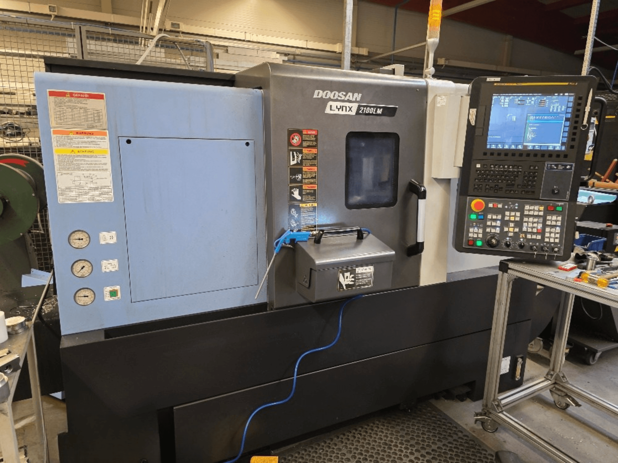 Tornio CNC Doosan Lynx 2100LM, vista frontale, con pannello di controllo, manometri e avvisi di sicurezza.