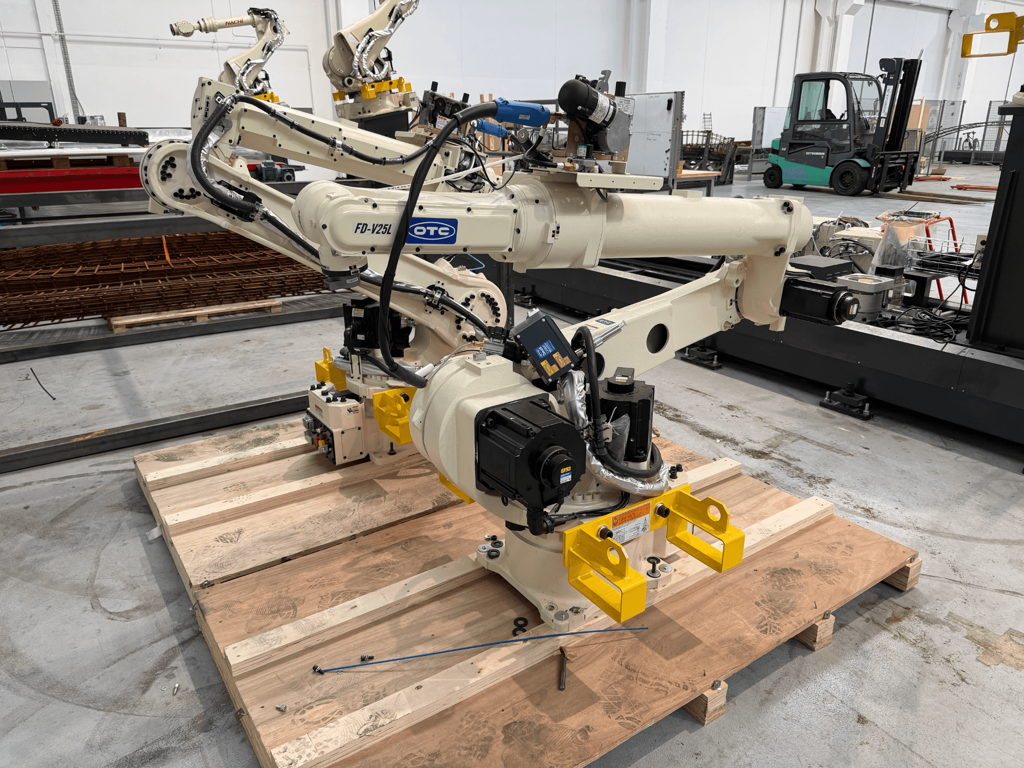 Braccio robotico OTC Daihen FD19-V25L visto frontalmente, con le pinze gialle e i componenti meccanici a vista, su un pallet di legno.