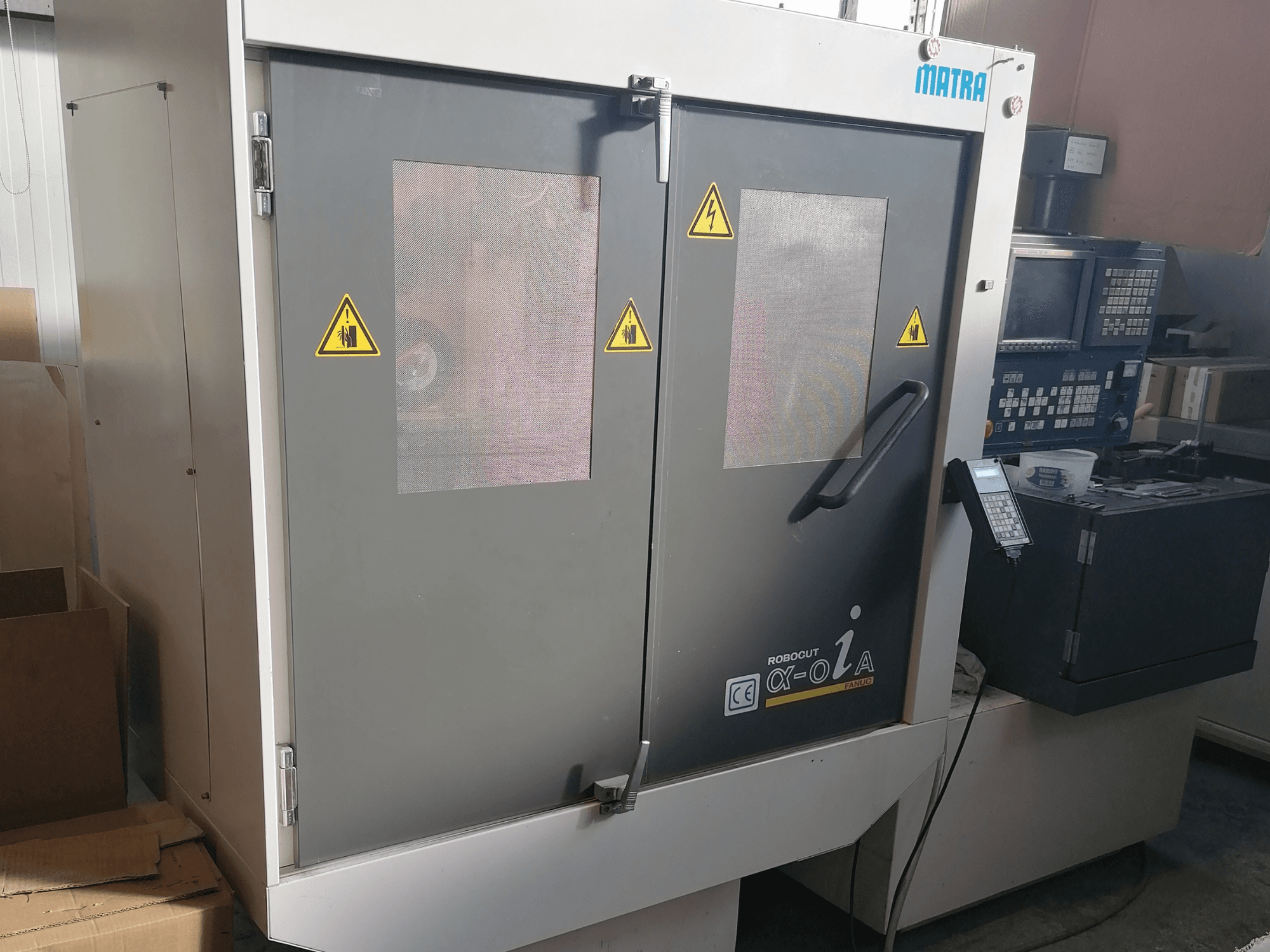 Macchina Robocut α-oZα di Matra, vista frontale che mostra le avvertenze di sicurezza, il pannello di controllo e le doppie porte con finestre a rete.