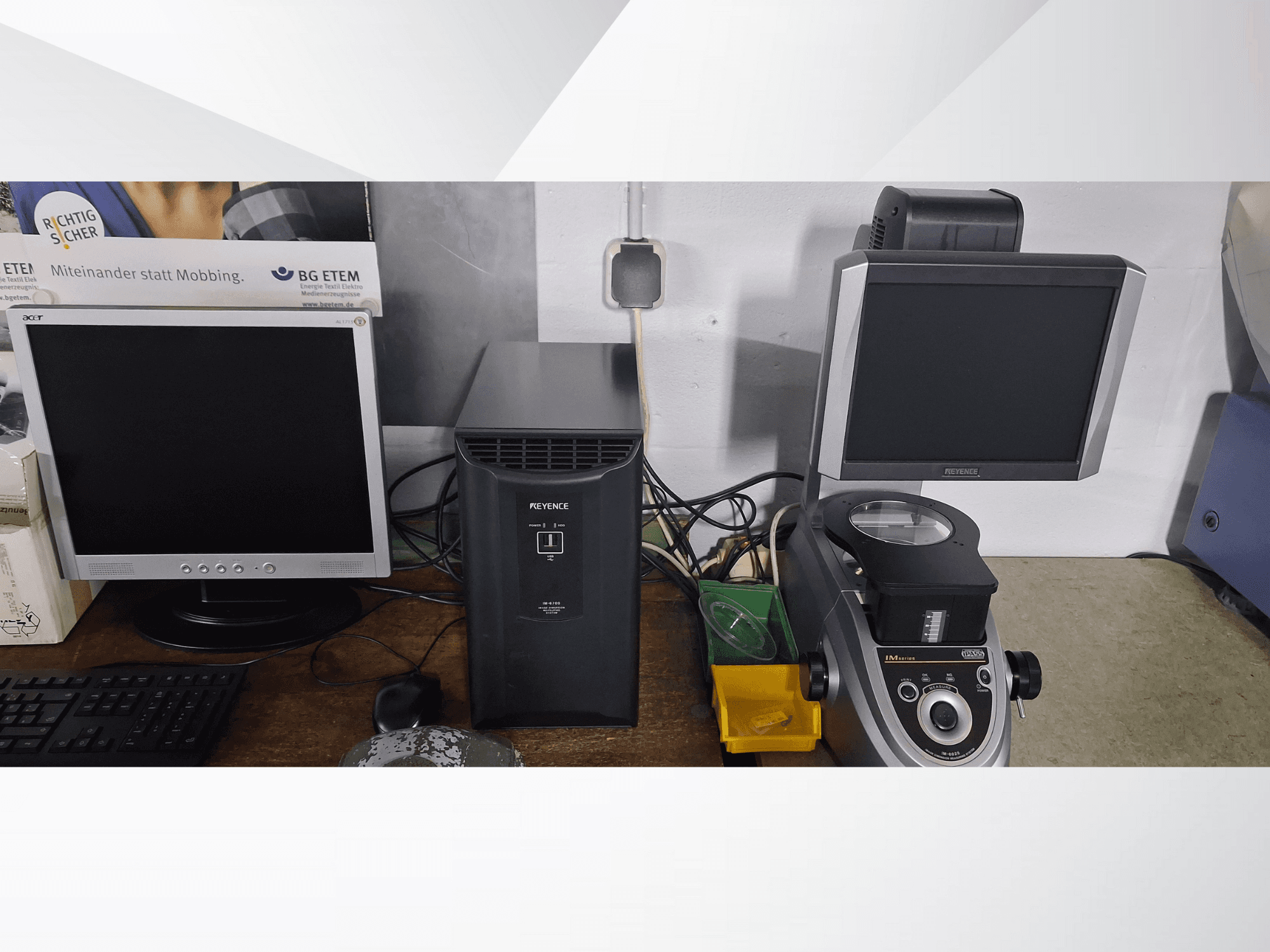 Due monitor di computer, uno Acer e uno Keyence, accanto a un dispositivo nero e a un microscopio, visti di fronte.