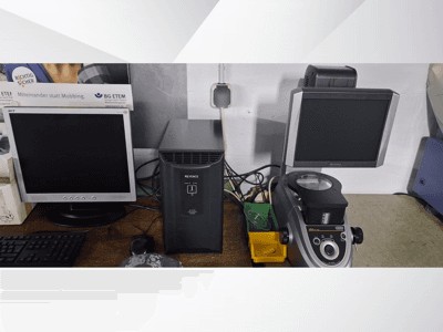 Due monitor di computer, uno Acer e uno Keyence, accanto a un dispositivo nero e a un microscopio, visti di fronte.