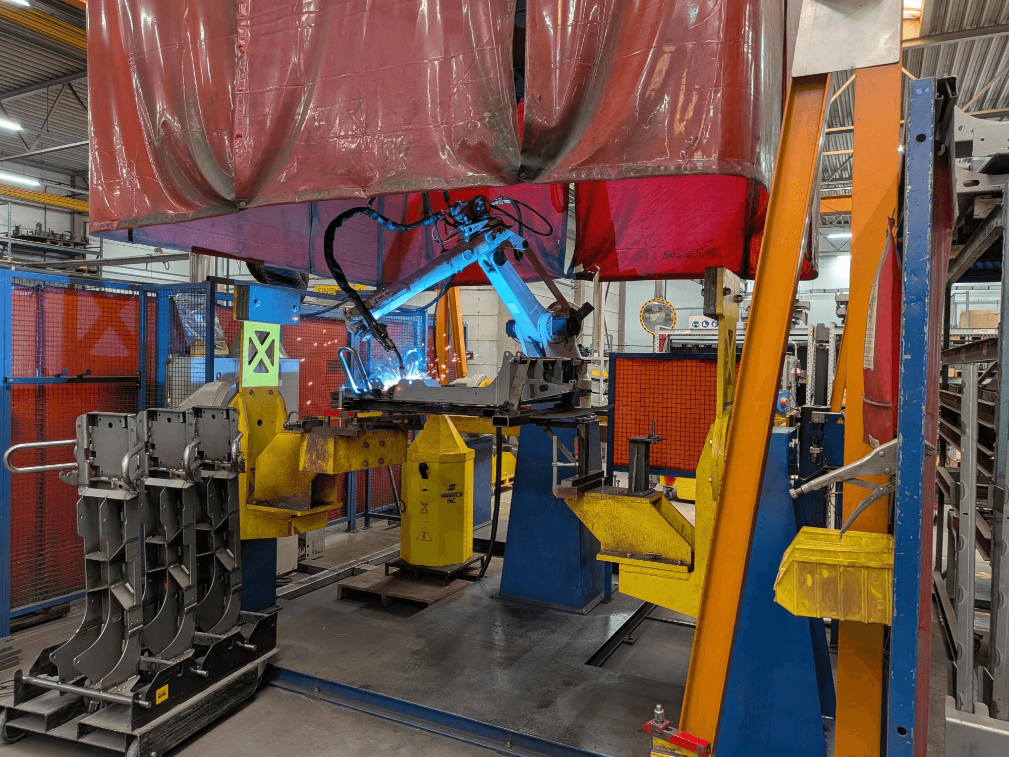Il robot di saldatura OTC Daihen DR4200 in azione, visto frontalmente, con l'arco di saldatura di colore blu brillante e la copertura protettiva.