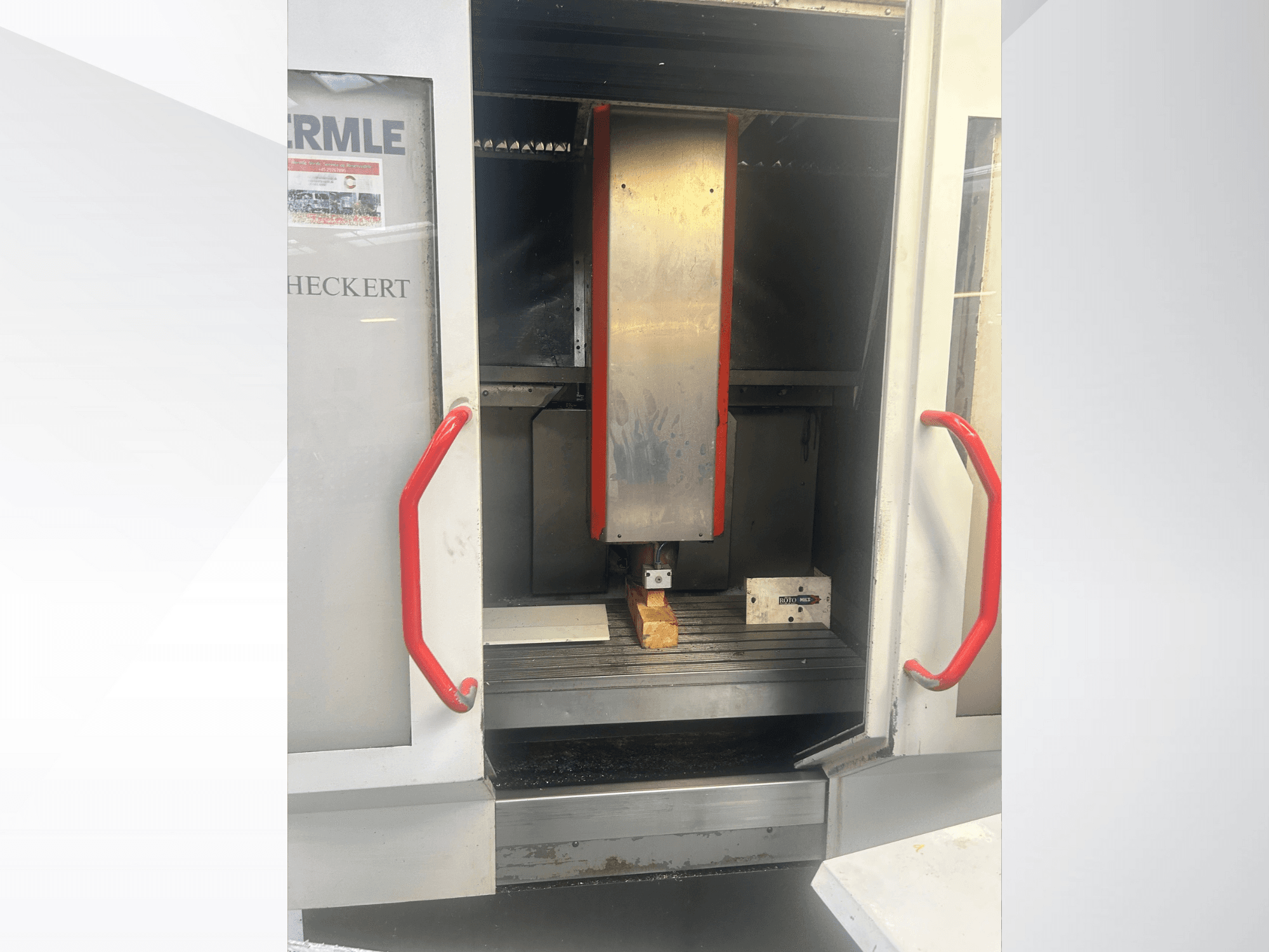 Vista frontale della macchina CNC Hermle, con interno metallico, maniglie rosse e pezzo in lavorazione sul tavolo.