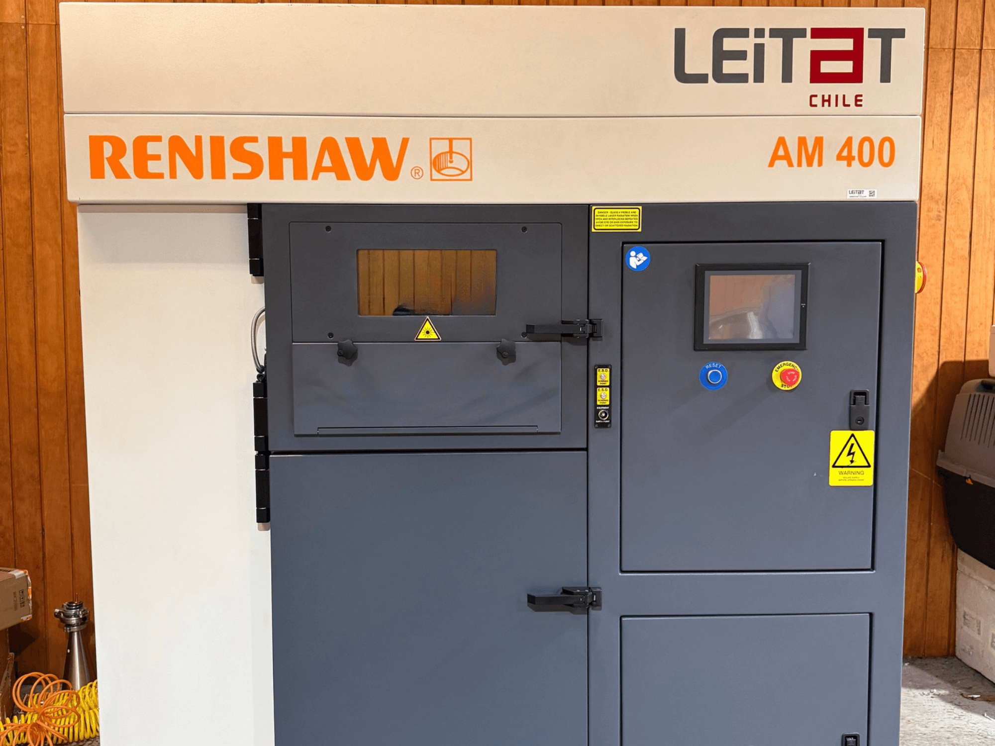 Vista frontale della stampante 3D per metalli RENISHAW AM400, con pannello di controllo, etichette di avvertenza e accesso per la manutenzione.