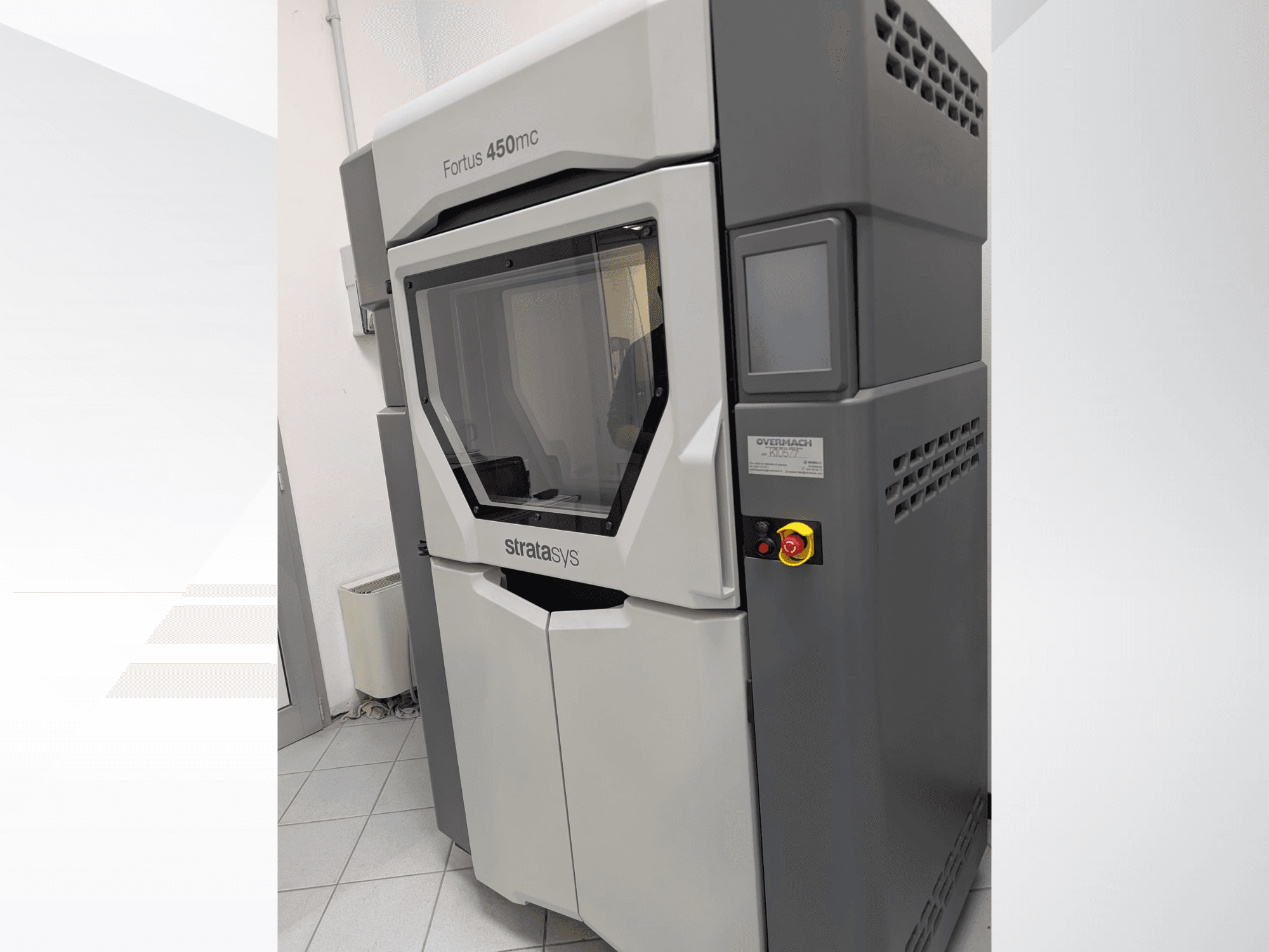La stampante 3D in plastica Fortus 450mc è mostrata in una vista laterale, con un pannello frontale trasparente e pulsanti di controllo sul lato.