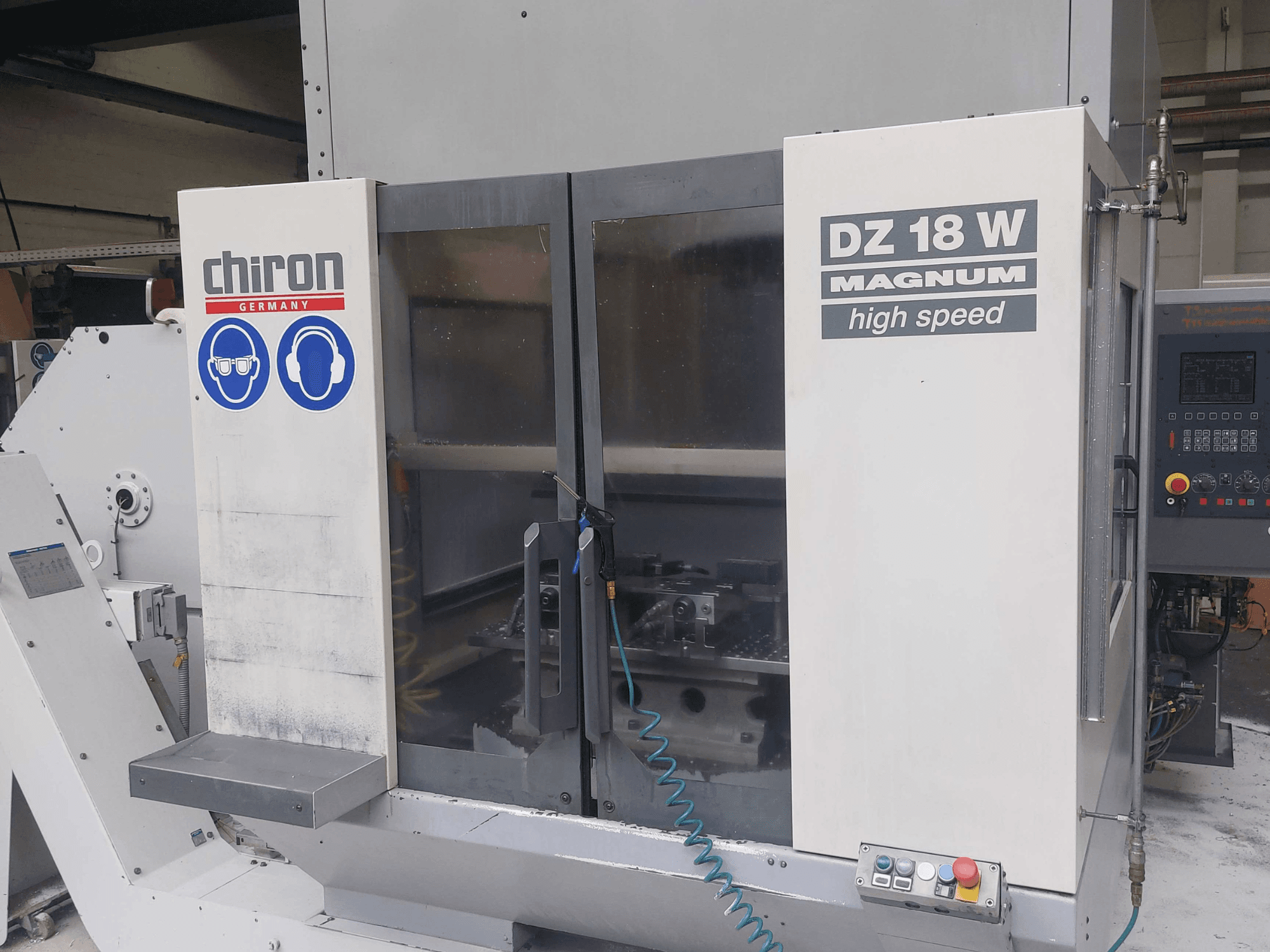 Centro di lavoro verticale CHIRON DZ 18 W MAGNUM, vista frontale con pannello di controllo e segnaletica di sicurezza.