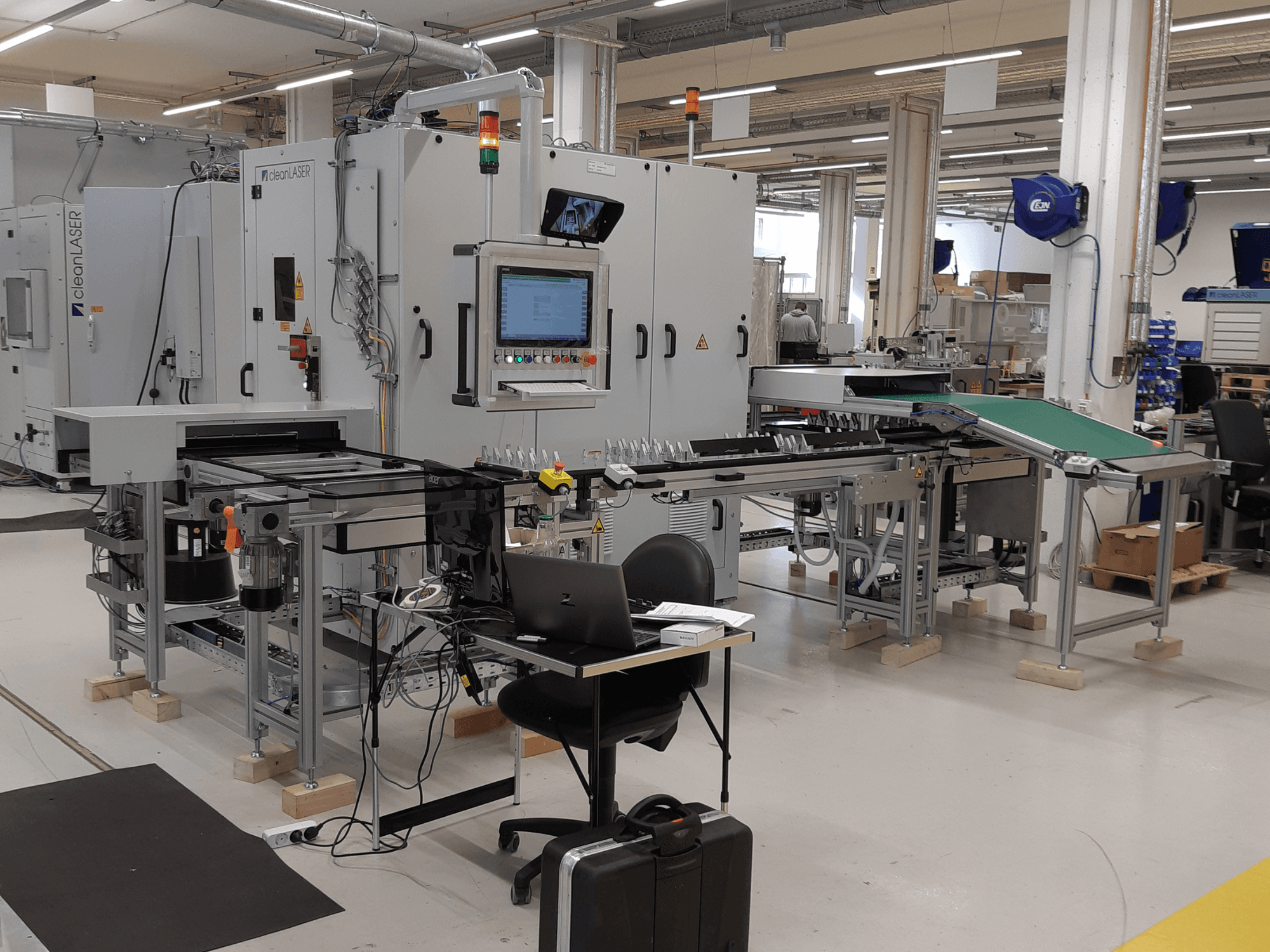 Macchina utensile CLEAN LASER clean CELL 3220 CL600, vista frontale, con pannello di controllo, nastro trasportatore e area di lavoro visibili in un ambiente di officina.