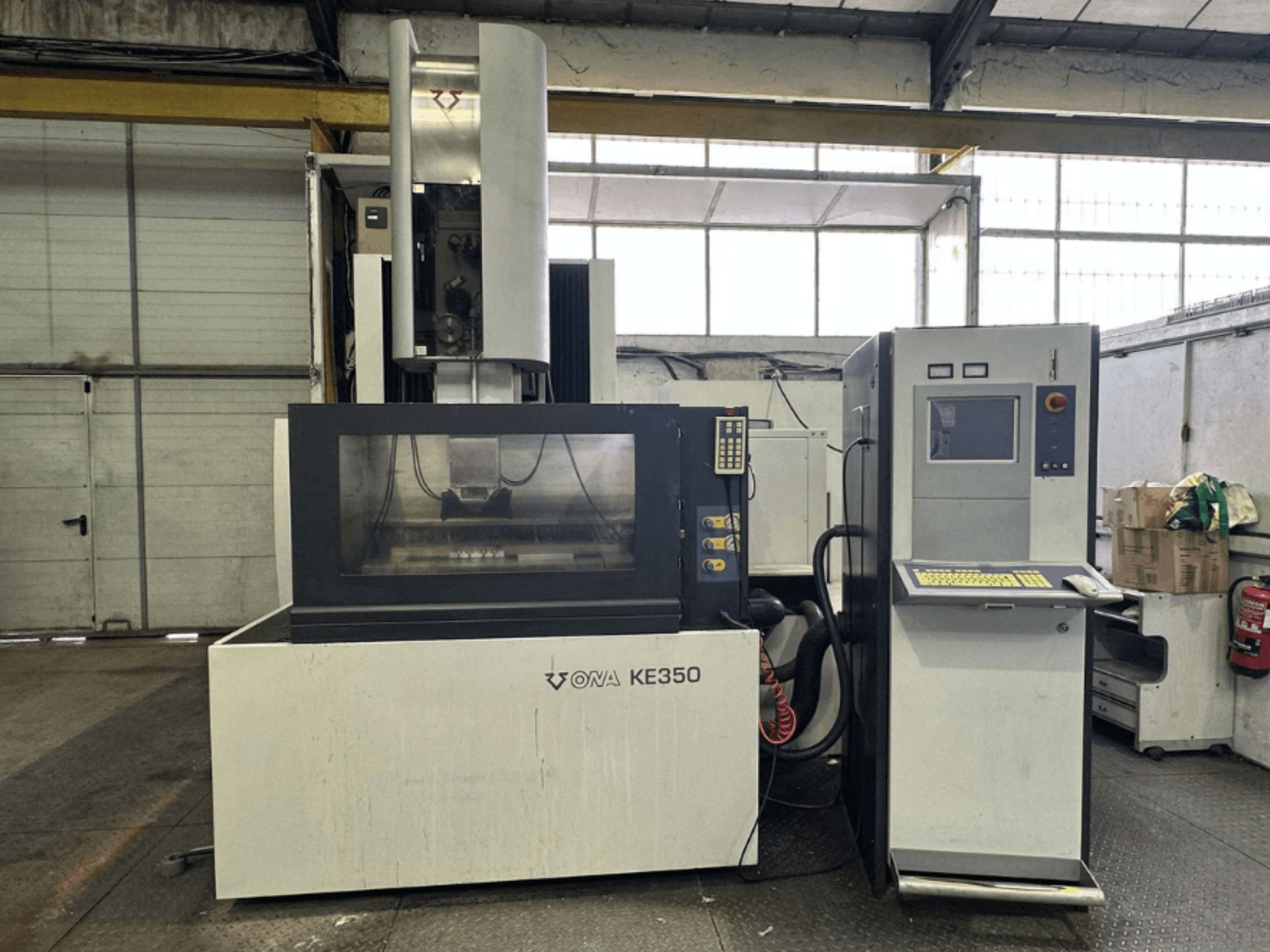 Vista frontale della macchina CNC ONA KE350 con pannello di controllo, schermo e vari pulsanti, situata in un ambiente industriale.