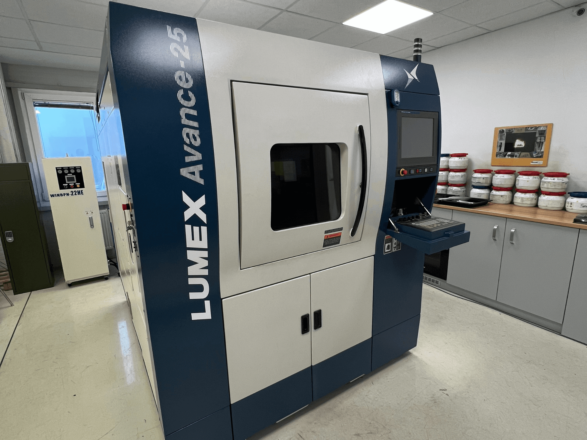 Stampante 3D LUMEX Avance-25 in un laboratorio, vista frontale. Pannello di controllo con schermo e pulsanti visibili, attrezzature sullo sfondo.