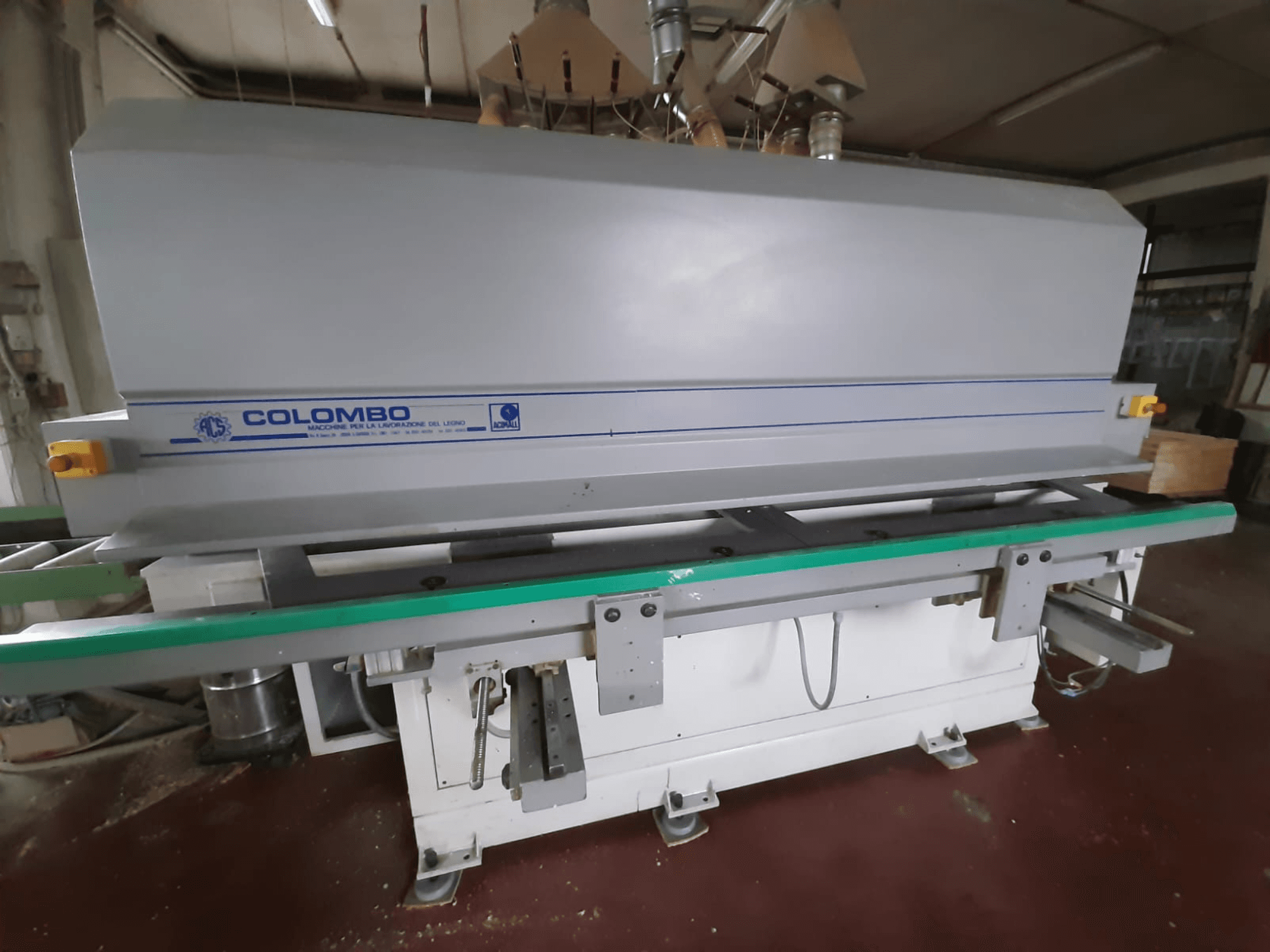 Macchina Colombo per la lavorazione del legno, vista frontale, con un lungo tavolo verde, pulsanti di controllo e un corpo grigio con accenti blu.