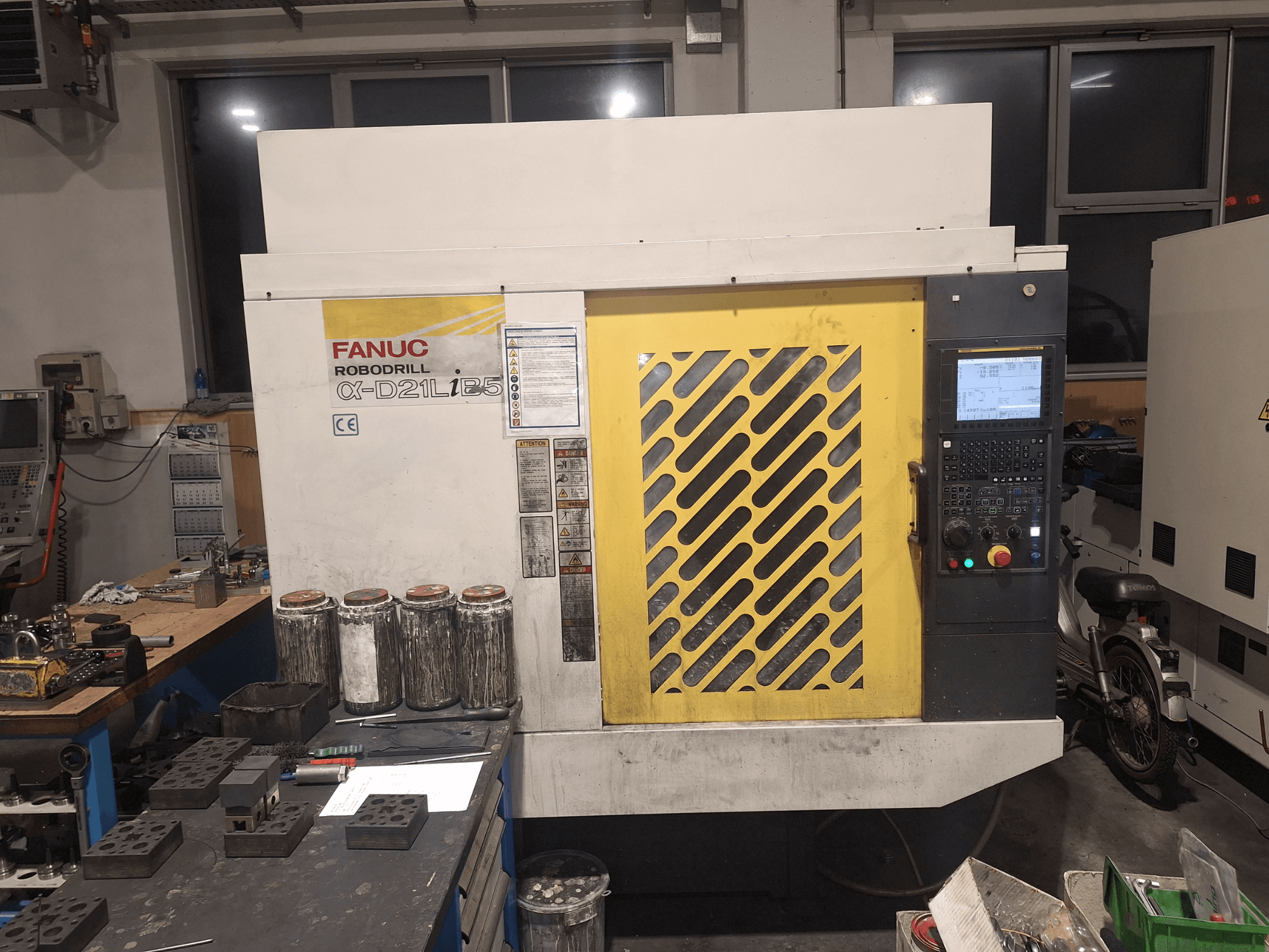 Vista frontale di FANUC Robodrill α-D21LiB5, che mostra il pannello di controllo, la griglia gialla e gli strumenti vicini su un banco di lavoro.