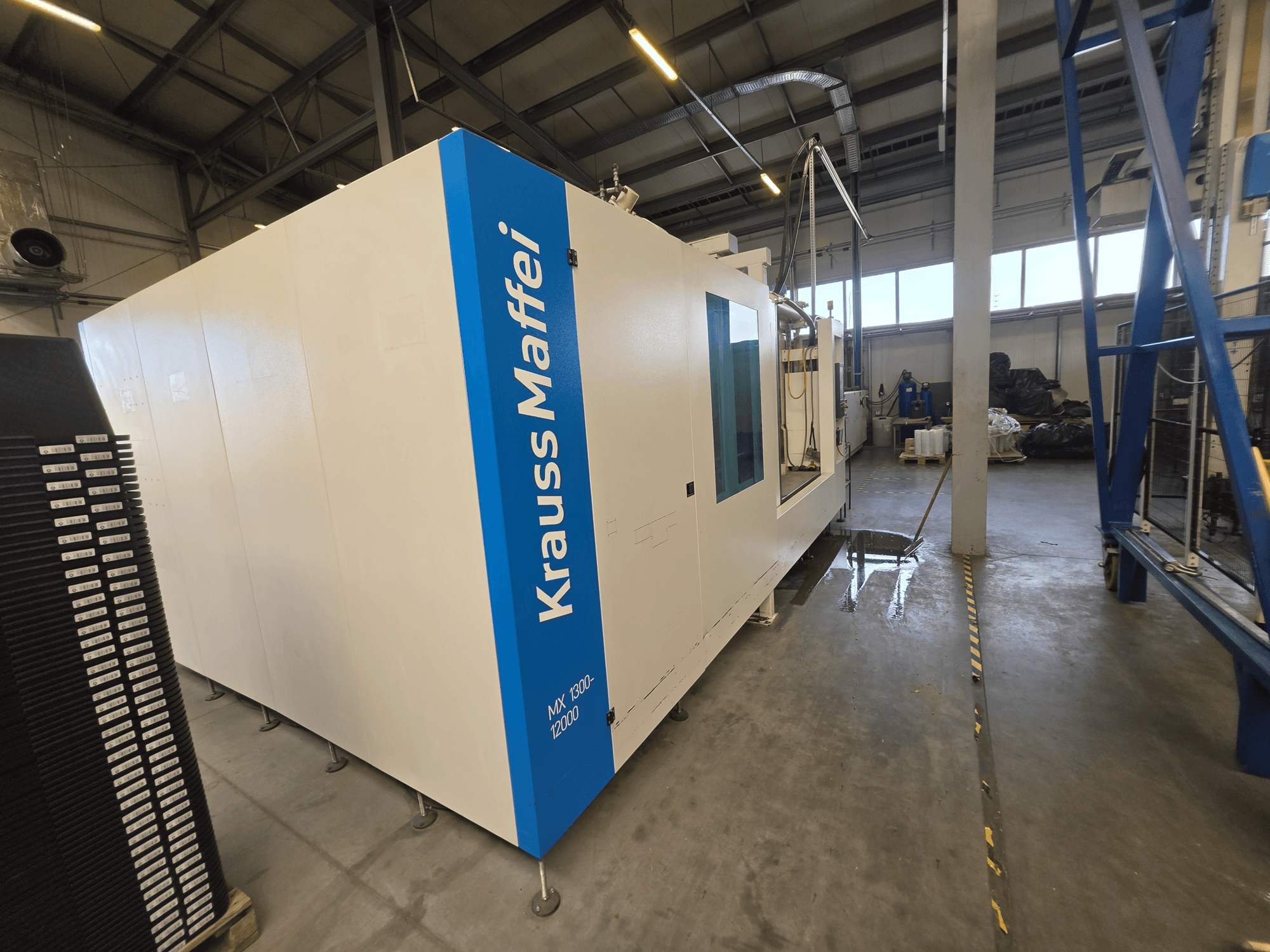 Macchina per stampaggio a iniezione idraulica Krauss Maffei MX 1300-12000 vista di profilo, che mette in risalto il suo ampio telaio bianco e il logo blu.