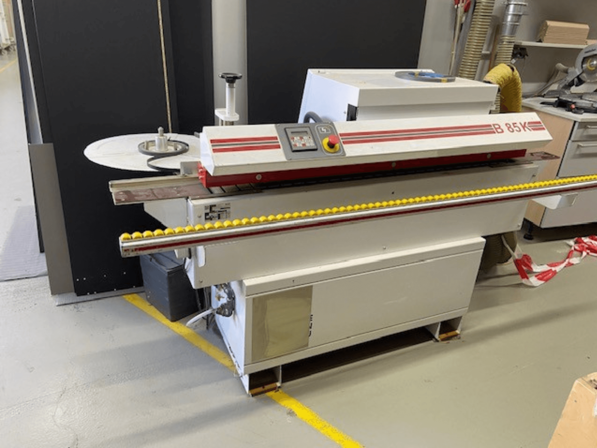 La bordatrice B 85K in bianco e rosso, vista frontale, presenta un pannello di controllo e un rullo giallo per l'alimentazione del materiale.