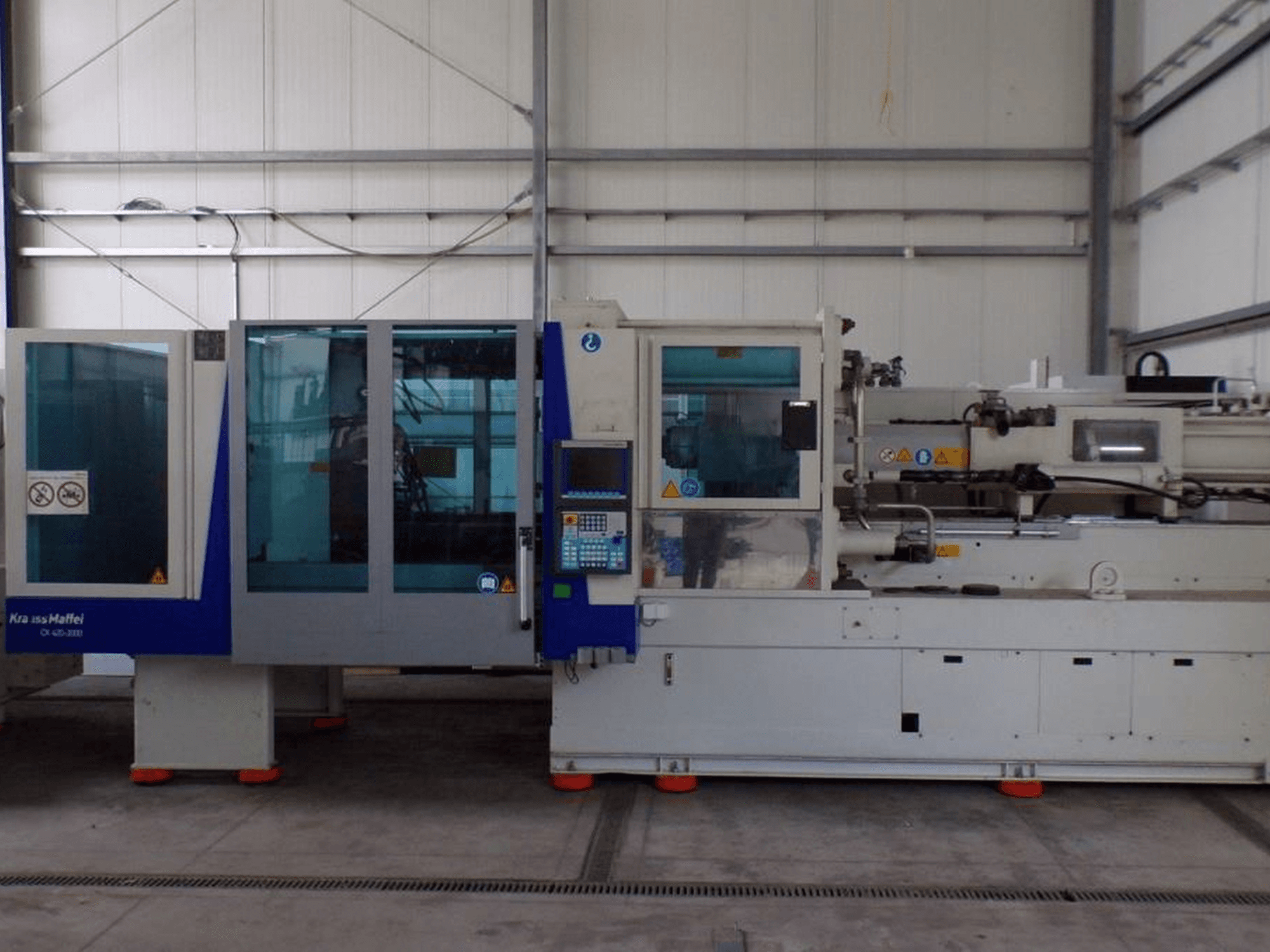 Macchina per lo stampaggio a iniezione KraussMaffei, vista laterale, con pannello di controllo e indicatori di sicurezza, visibile in fabbrica.