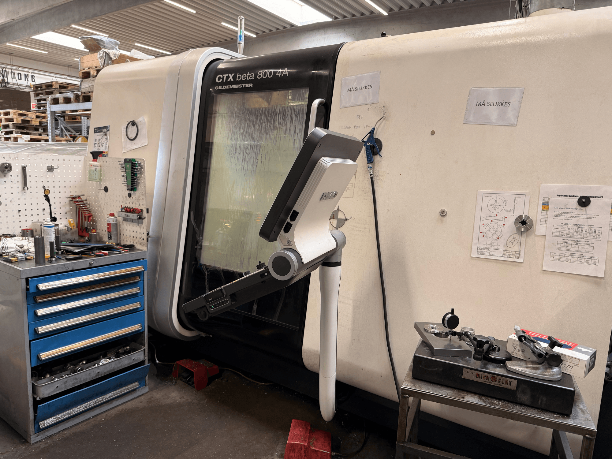 Tornio verticale DMG MORI CTX Beta 800 4a in un'officina, con braccio di comando e documenti tecnici nelle vicinanze.