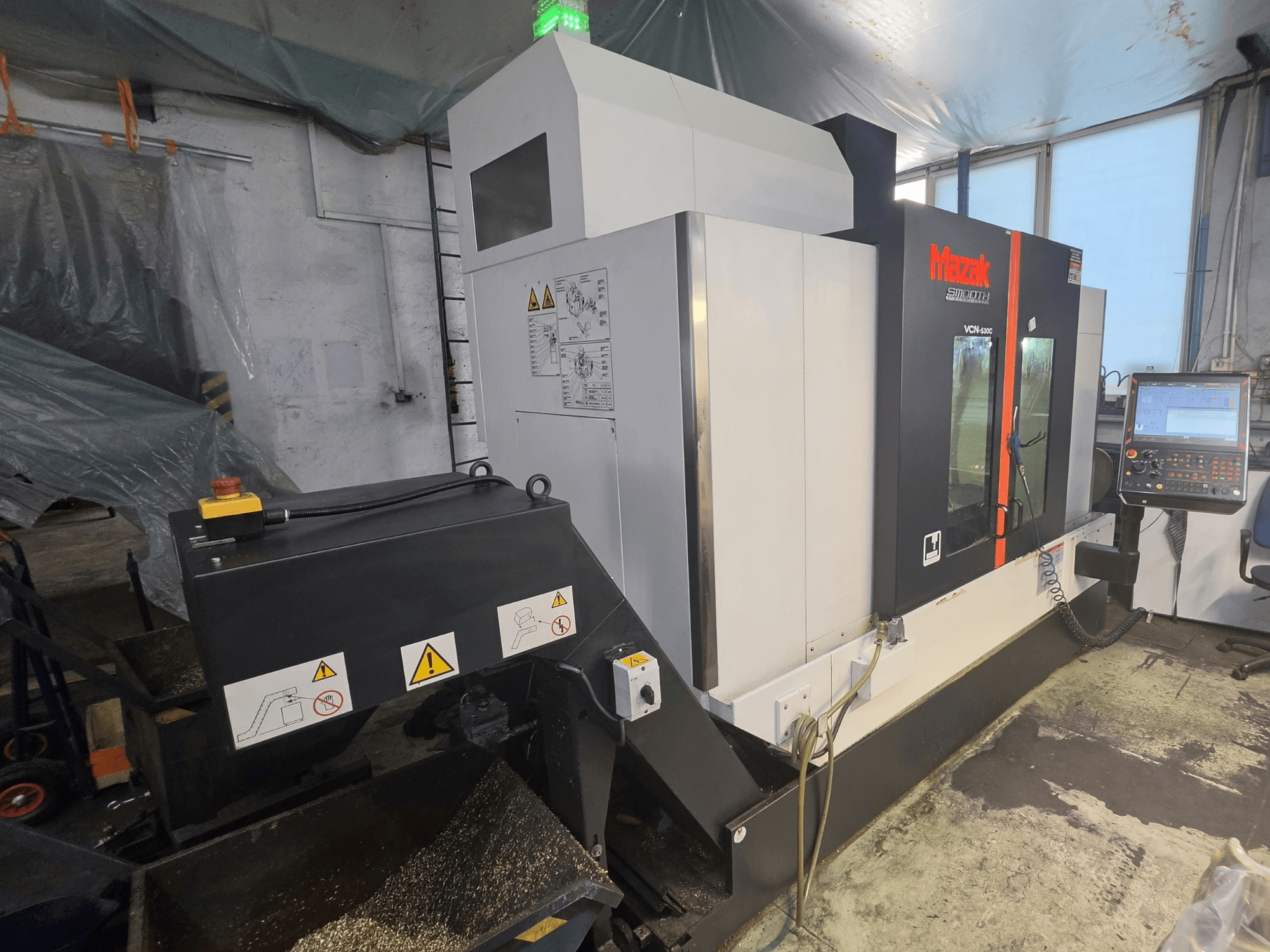 Vista frontale del centro di lavorazione verticale Mazak VCN-530C, con pannello di controllo, catena degli utensili e indicatori di funzionamento.