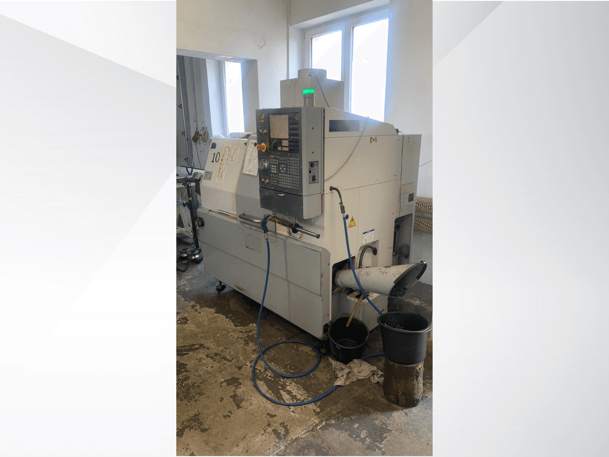 Modello di macchina CNC Haas con pannello di controllo, vista laterale, con linea del refrigerante, scivolo di scarico e contenitori di stoccaggio sottostanti.