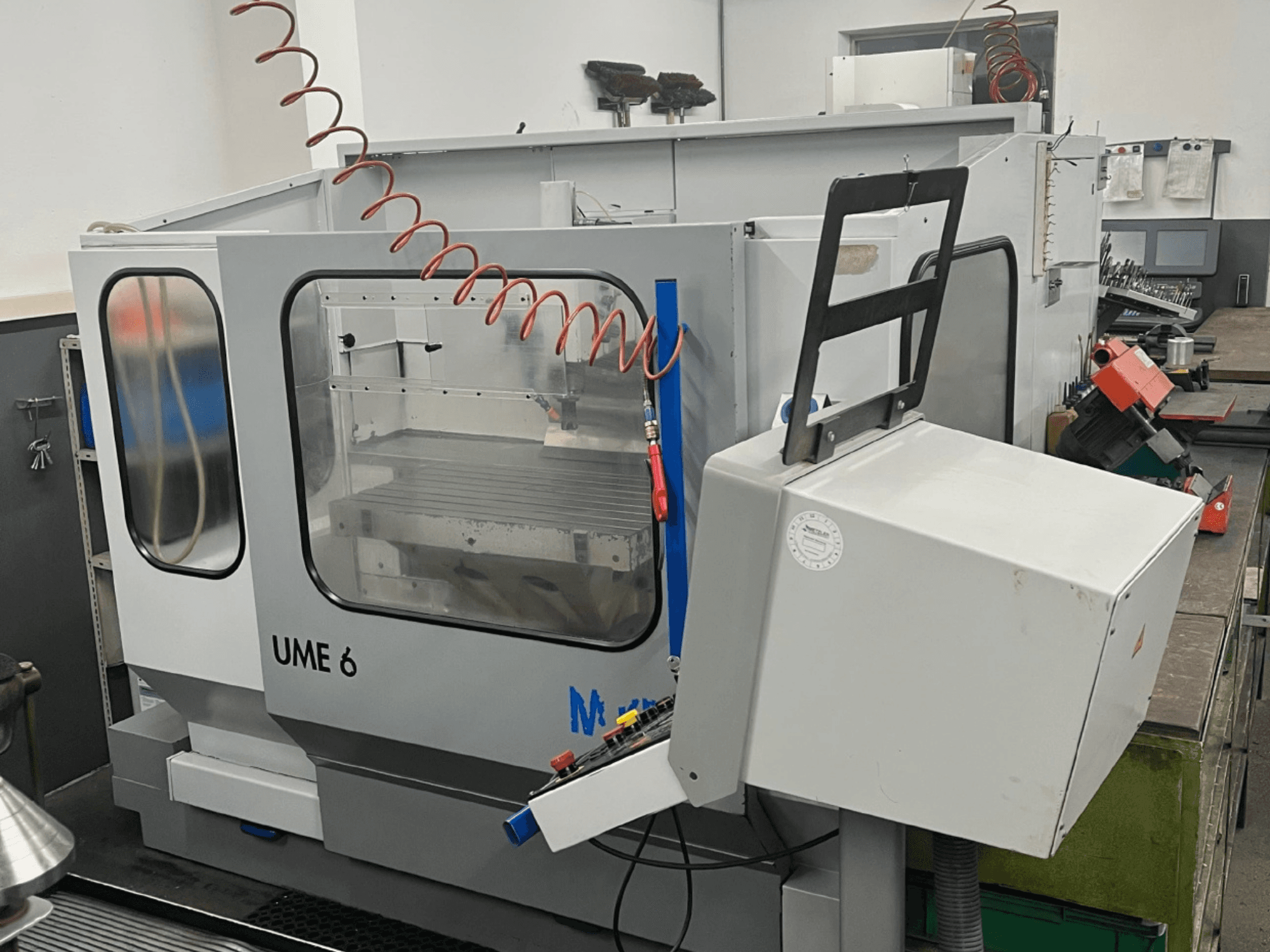 Centro di lavoro universale MIKRON UME600 in un'officina, vista laterale che mostra il pannello di controllo e il contenitore di protezione.