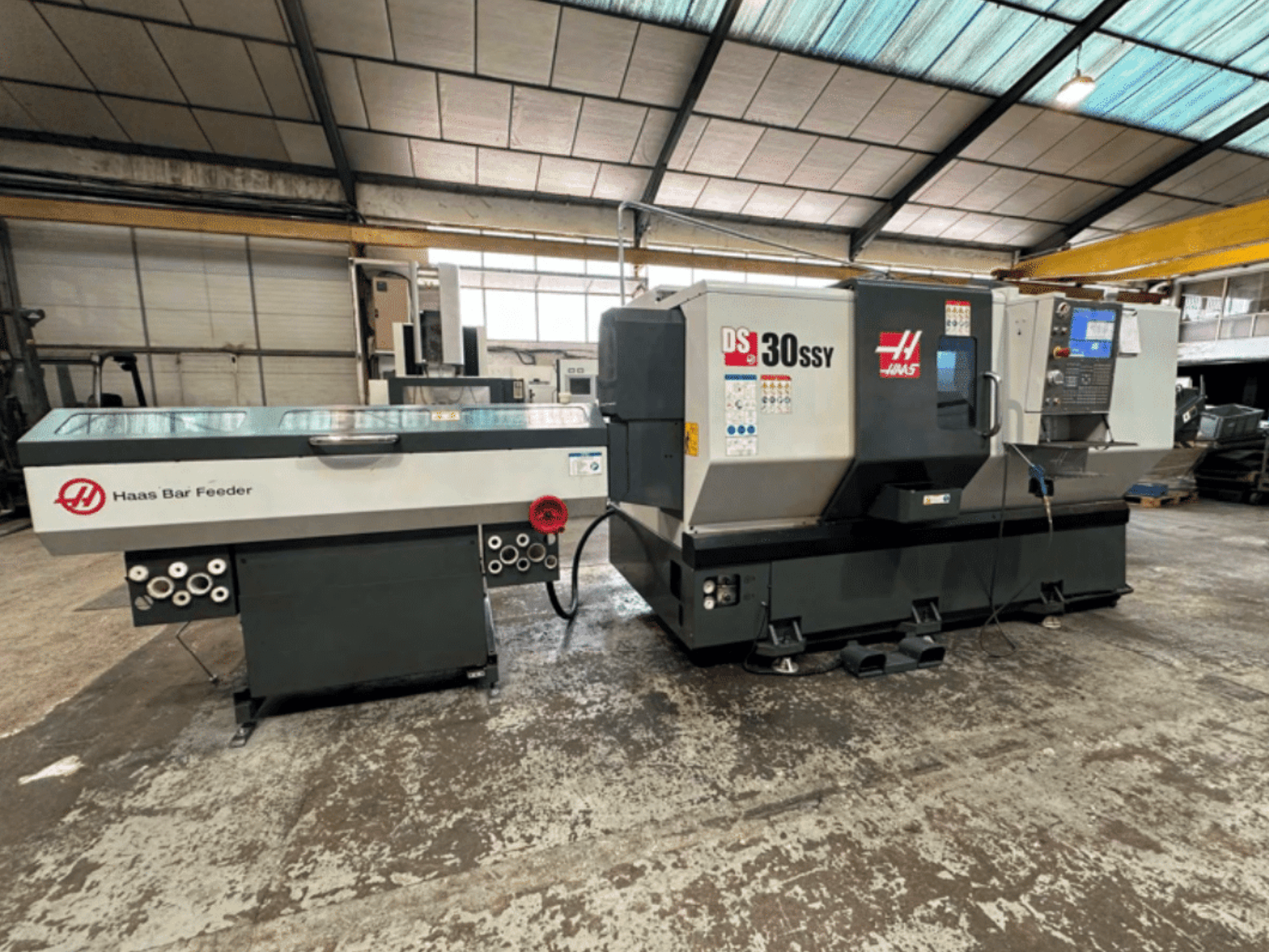 Tornio CNC Haas DS-30SSY con caricatore di barre Haas, vista laterale che mostra il pannello di controllo e il meccanismo di alimentazione in un'officina.