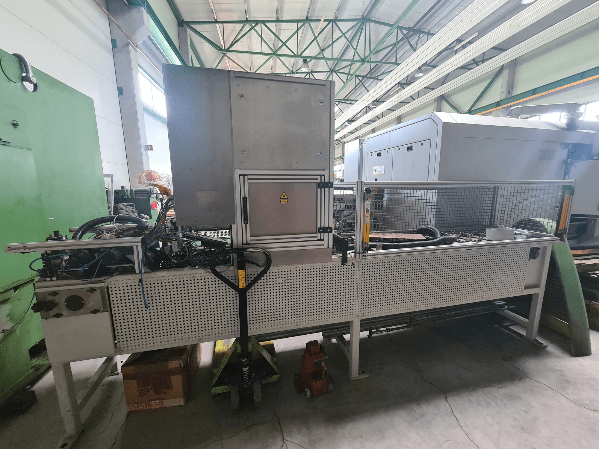 Macchinario industriale con struttura metallica, tubi e pannello di controllo, visto di lato in una fabbrica.