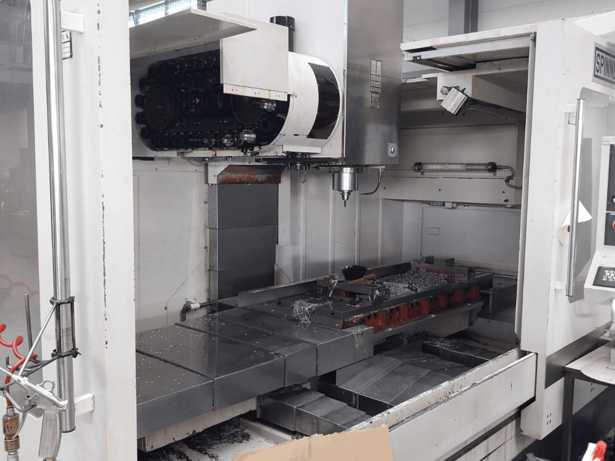Vista frontale del centro di lavoro verticale SPINNER MVC 1600 che mostra l'area di lavoro aperta, il mandrino e i trucioli di metallo sul tavolo.