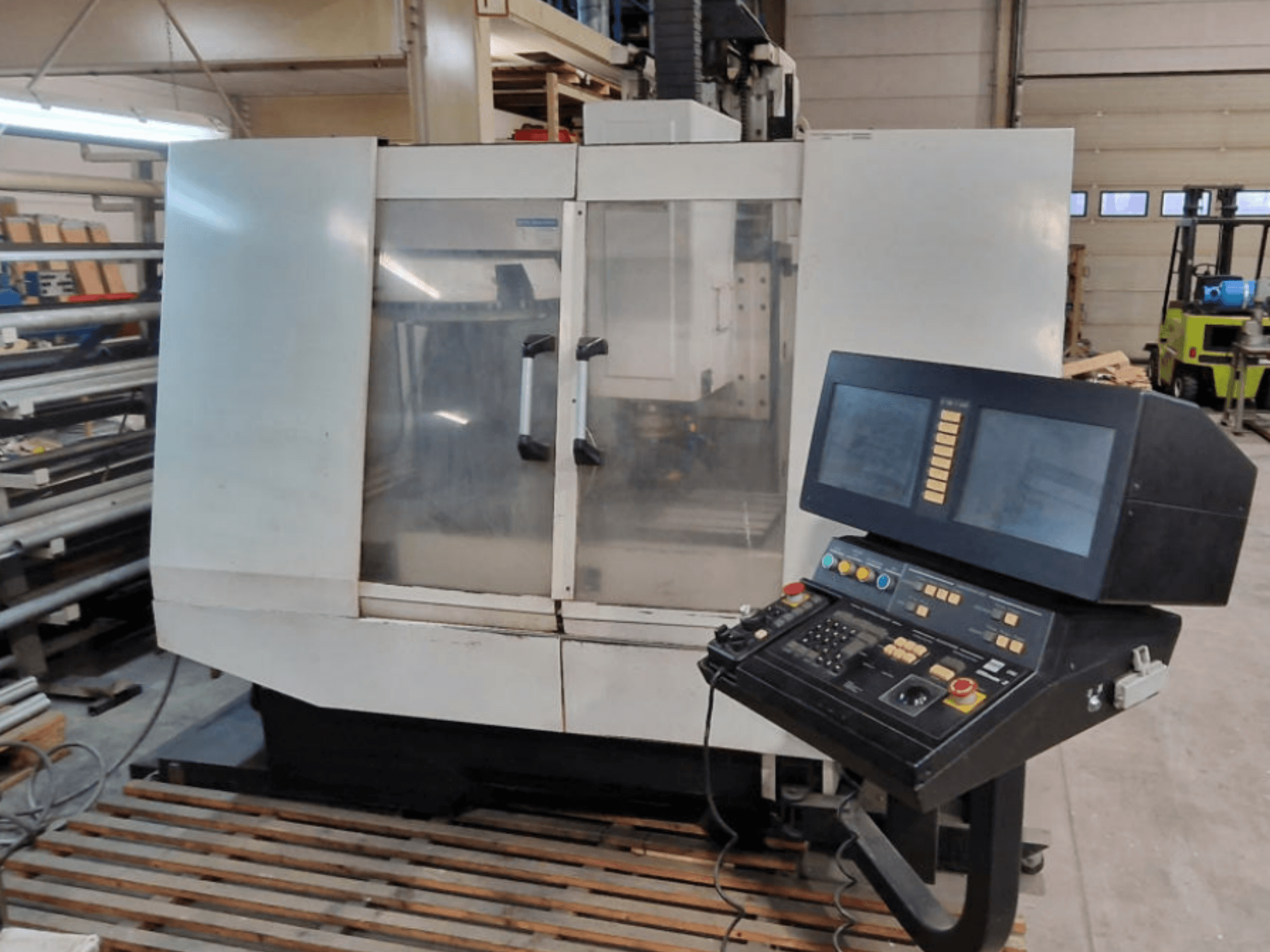 Centro di lavorazione verticale Hurco BMC30AP, vista frontale che mostra il pannello di controllo con pulsanti e schermi, su un pallet di legno.
