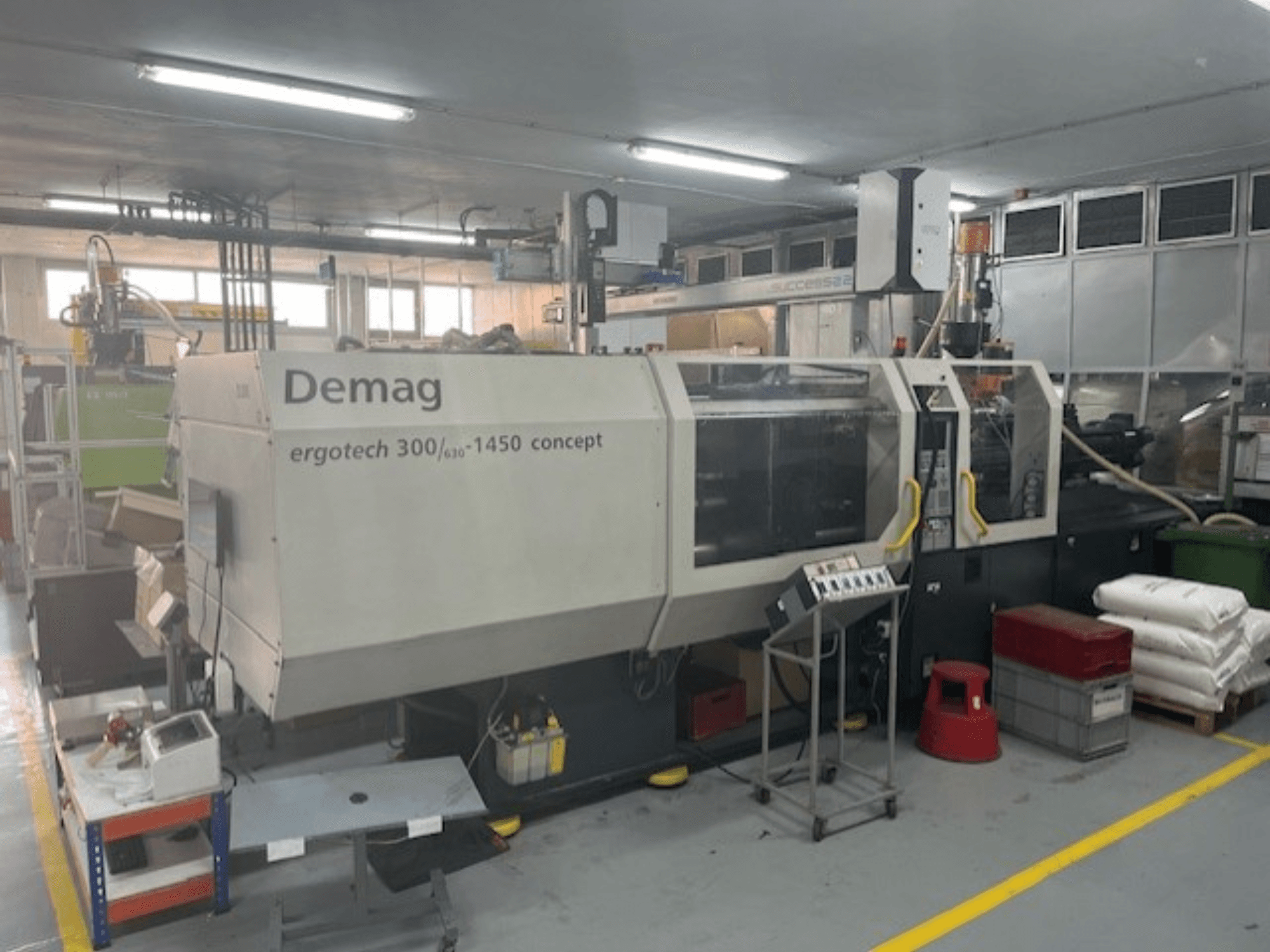 Pressa a iniezione idraulica Demag ERGOTECH CONCEPT 3000-1450, vista frontale, con comandi operativi e materiali vicini.