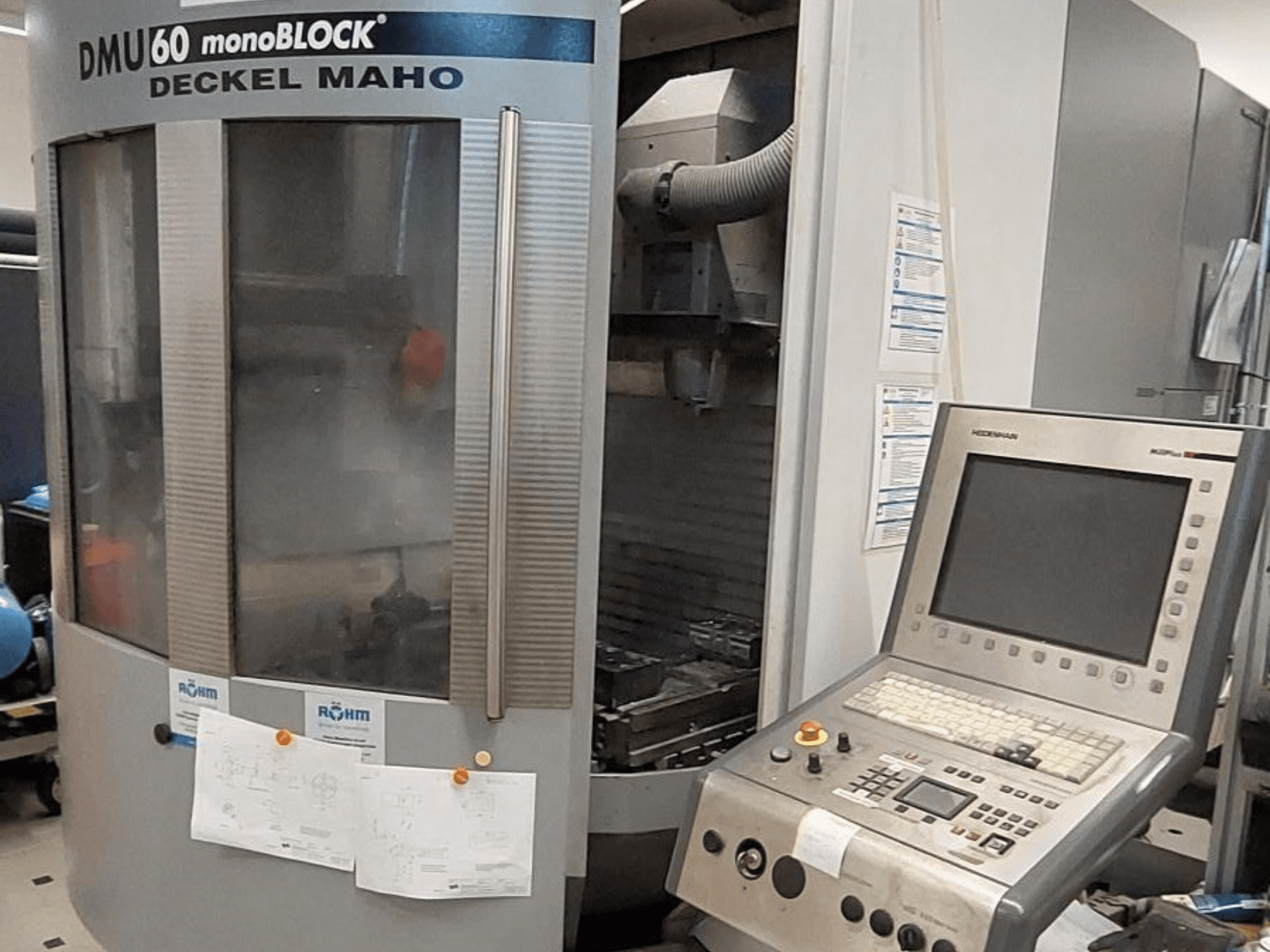 DMU 60 monoBLOCK di Deckel Maho, vista frontale di una fresatrice CNC con pannello di controllo e disegni tecnici allegati.