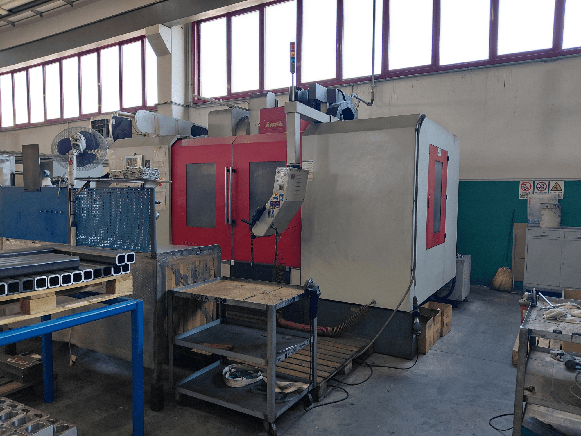 Centro di lavorazione verticale AWEA BM-1600, vista frontale, con struttura rossa e grigia; in primo piano sono visibili il banco da lavoro e gli utensili.