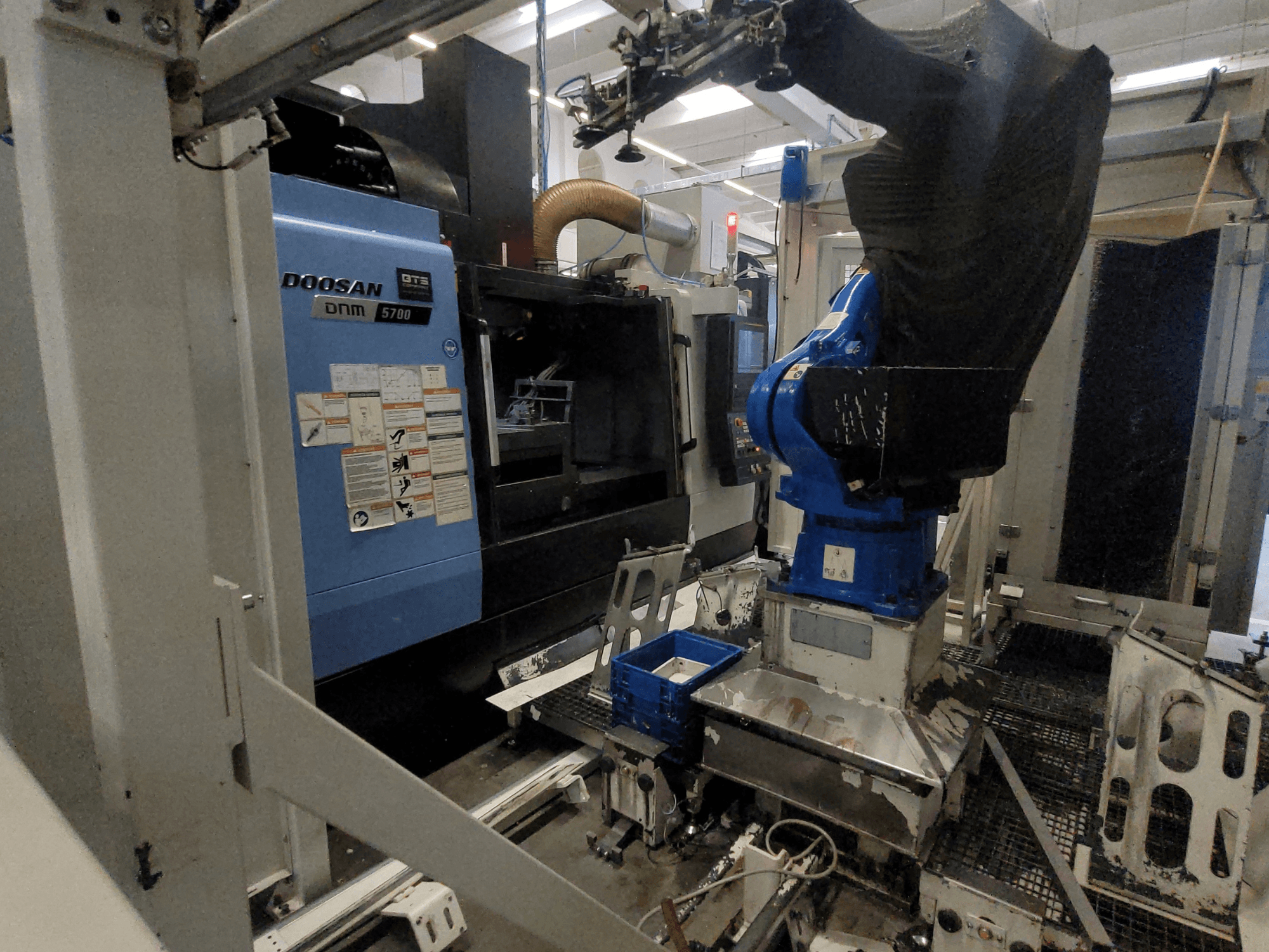 Centro di lavorazione verticale DOOSAN DNM 5700 in un ambiente industriale, con vista frontale e integrazione del braccio robotico.