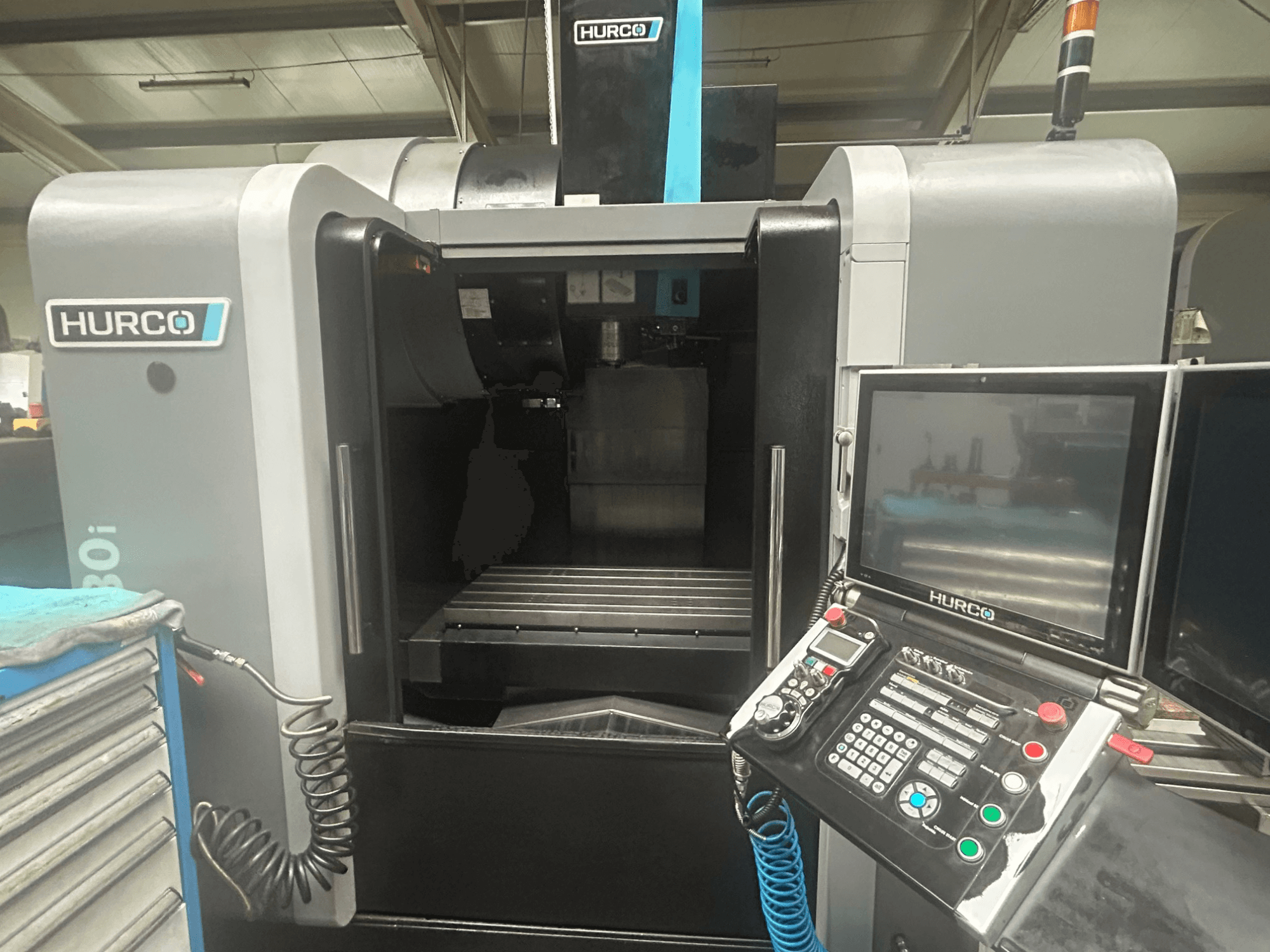 Vista frontale della macchina CNC Hurco VM30i, con pannello di controllo con pulsanti, display e area di stoccaggio utensili.