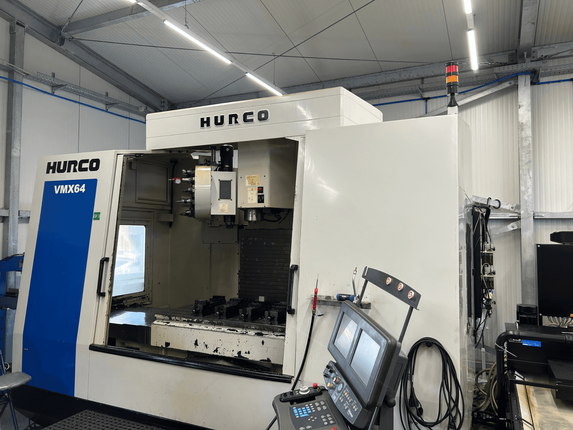 Centro di lavorazione verticale Hurco VMX 64, vista frontale, che mostra il pannello di controllo e l'area di lavoro aperta con gli utensili.