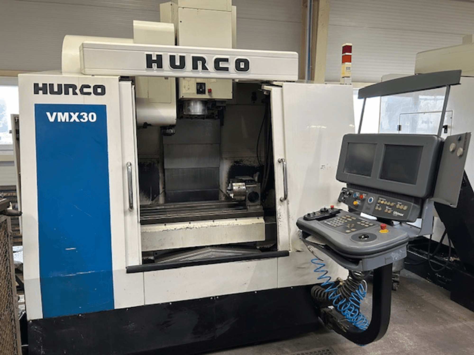 Fresatrice CNC Hurco VMX30 in un'officina, vista frontale; presenta un pannello di controllo con doppio schermo e pulsanti operativi.