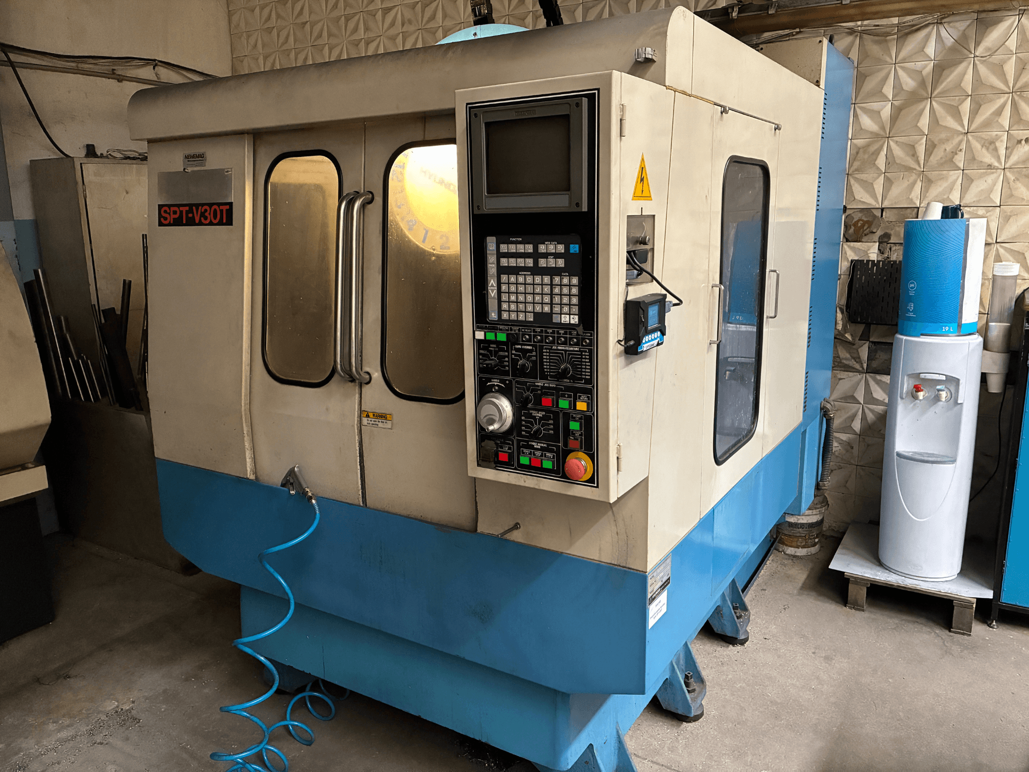 Macchina CNC SPT-V30T in blu e bianco, vista frontale che mostra il pannello di controllo, le porte e il tubo dell'aria. Perfetta per lavorazioni di precisione.