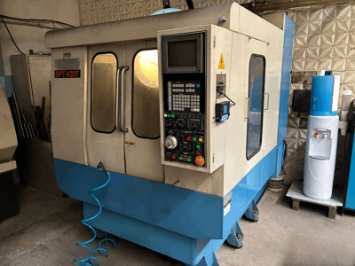 Macchina CNC SPT-V30T in blu e bianco, vista frontale che mostra il pannello di controllo, le porte e il tubo dell'aria. Perfetta per lavorazioni di precisione.