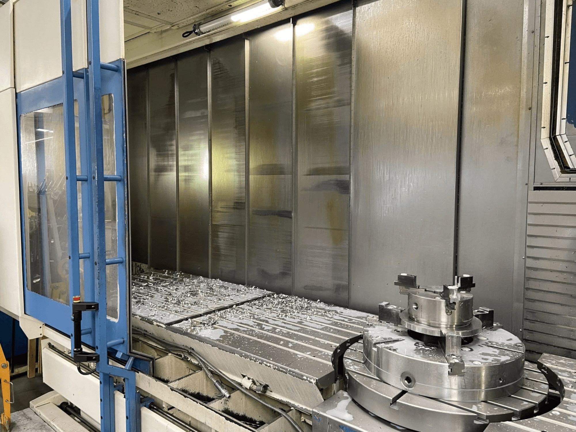Centro di lavorazione verticale AXA VHC-3-3000-M/E, vista frontale, con trucioli metallici fresati sul piano di lavoro e utensili da taglio.