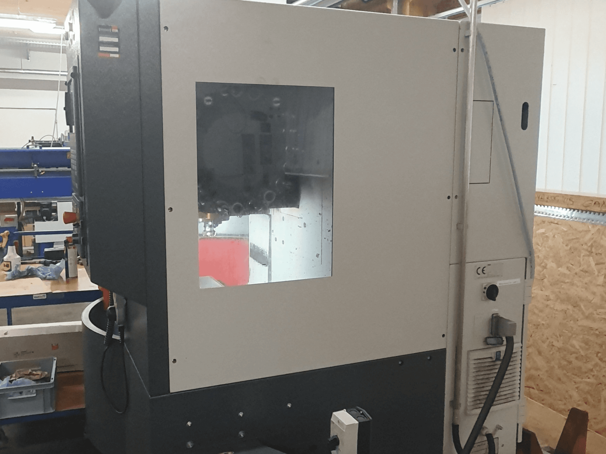 Vista laterale di una macchina per la lavorazione dei metalli con pannello di controllo visibile, ampia finestra di visualizzazione e intricati componenti interni.