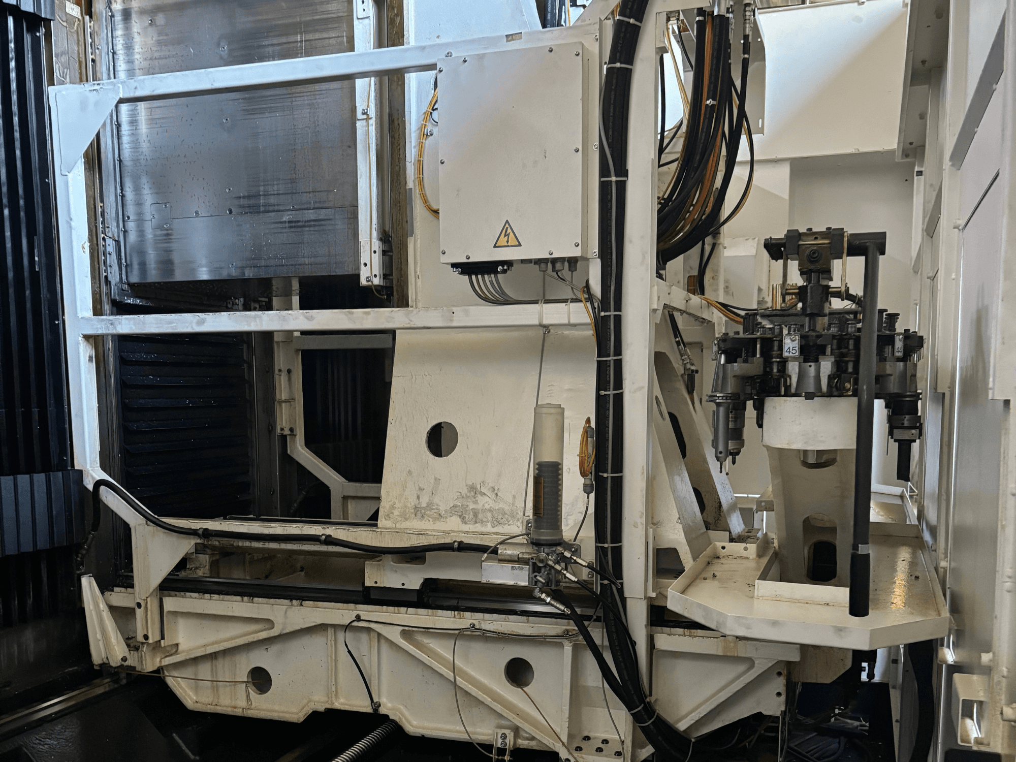 Vista laterale di una macchina industriale che mostra una fresatrice CNC bianca con utensili, tubi e pannello di controllo visibili.