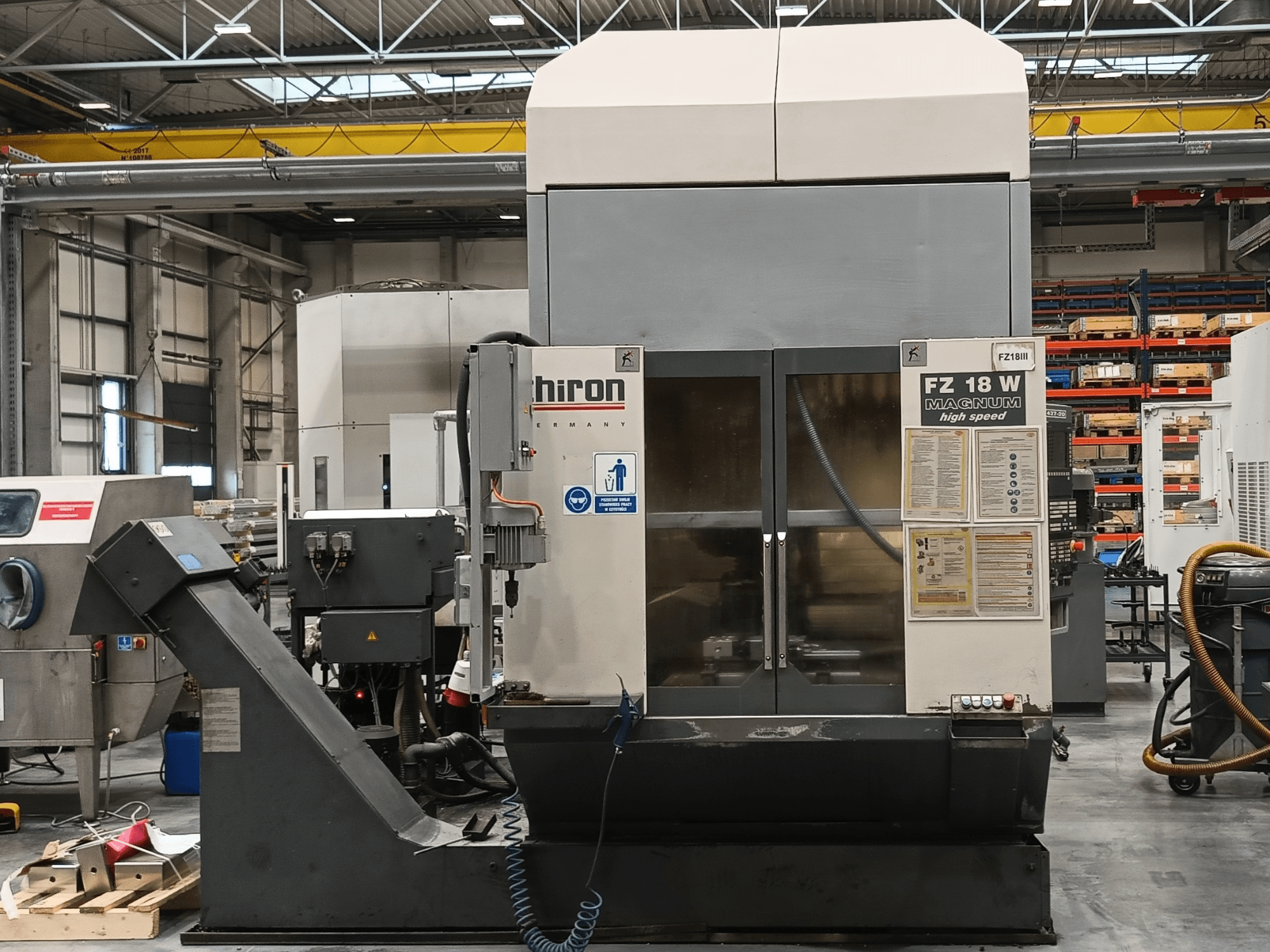 Macchina CNC Hiron FZ 18 W Magnum, vista frontale, con comandi, etichette di sicurezza e ambientazione industriale con utensili.