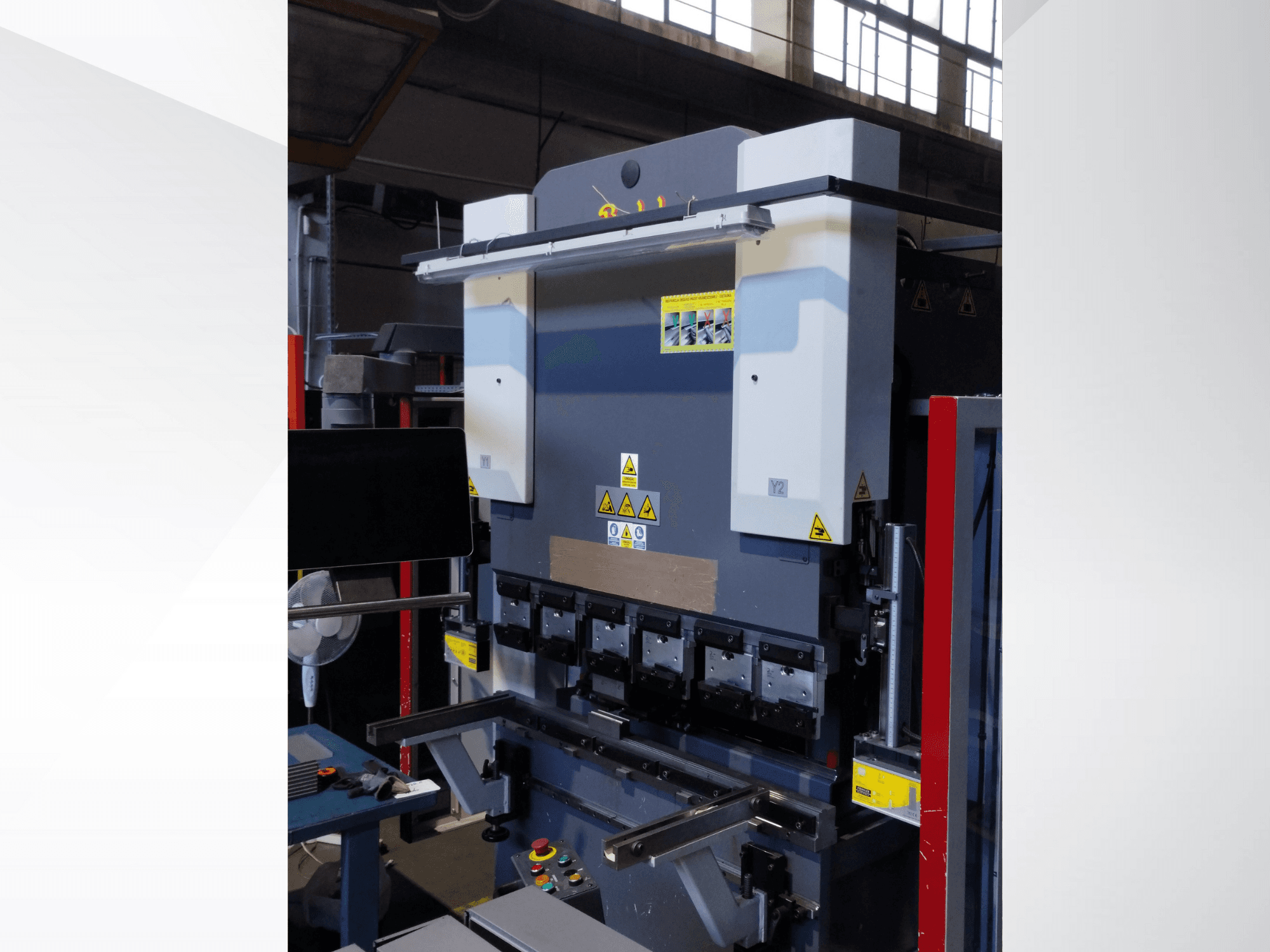 Macchina pressa piegatrice, vista frontale. Presenta comandi visibili, adesivi di sicurezza e porta stampi multipli per una piegatura di precisione.