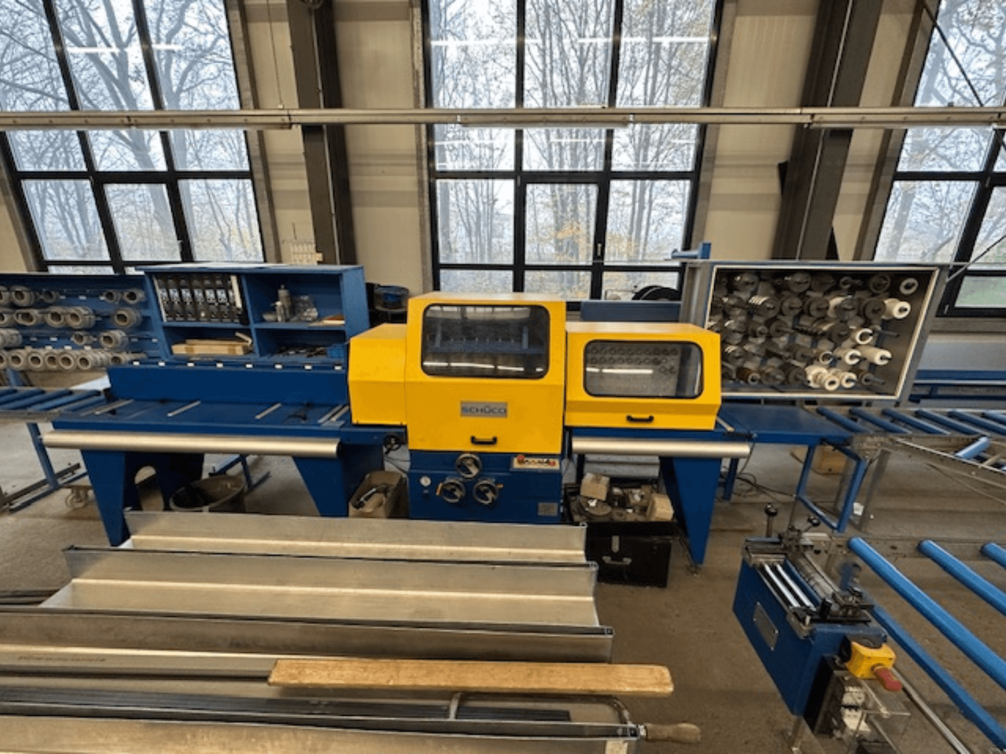 Vista frontale della macchina utensile SCHÜCO ISOMAT 4, con pannello di controllo giallo, rulli multipli e vano portaoggetti.