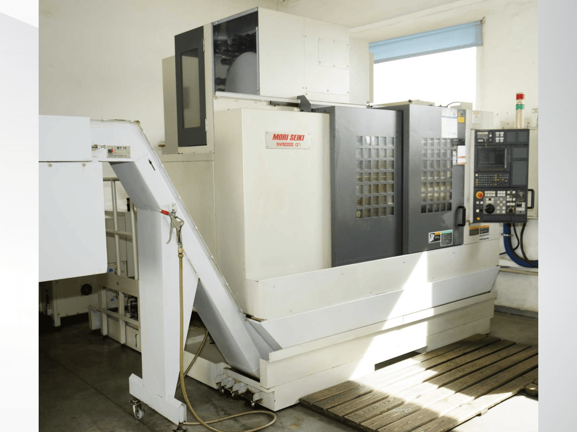 Centro di lavorazione verticale MORI SEIKI NV 5000 alpha1 in vista frontale, con in primo piano il pannello di controllo, i dispositivi di sicurezza e l'area di carico.
