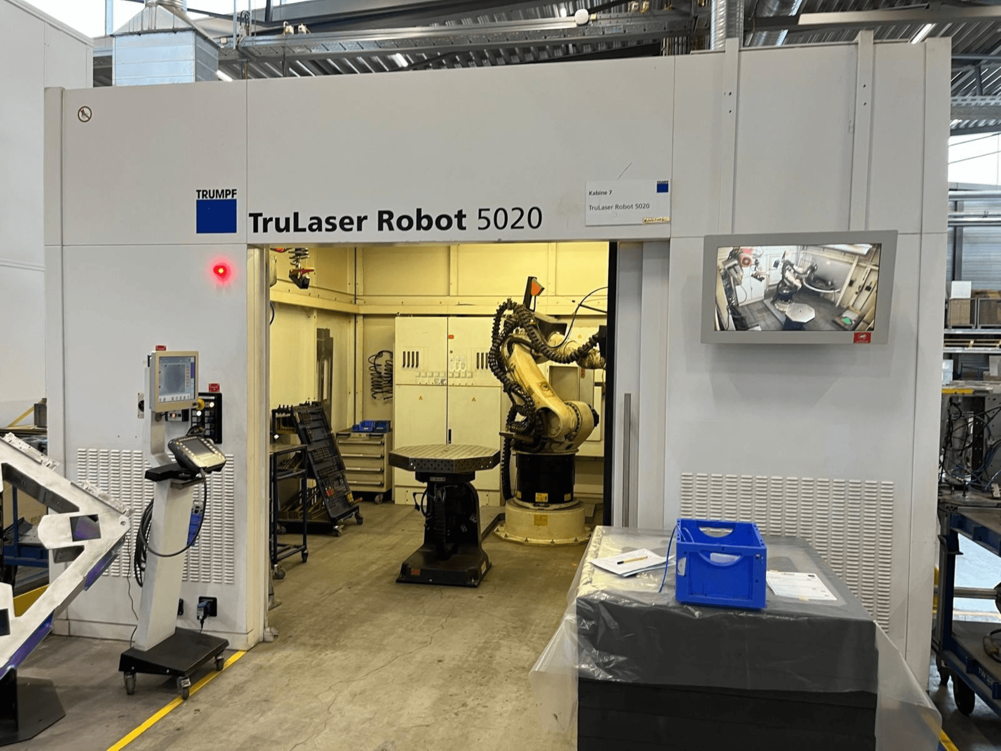 TRUMPF TruLaser Robot 5020 in un ambiente industriale, con i comandi, un braccio robotico e un monitor che mostra le operazioni in corso.