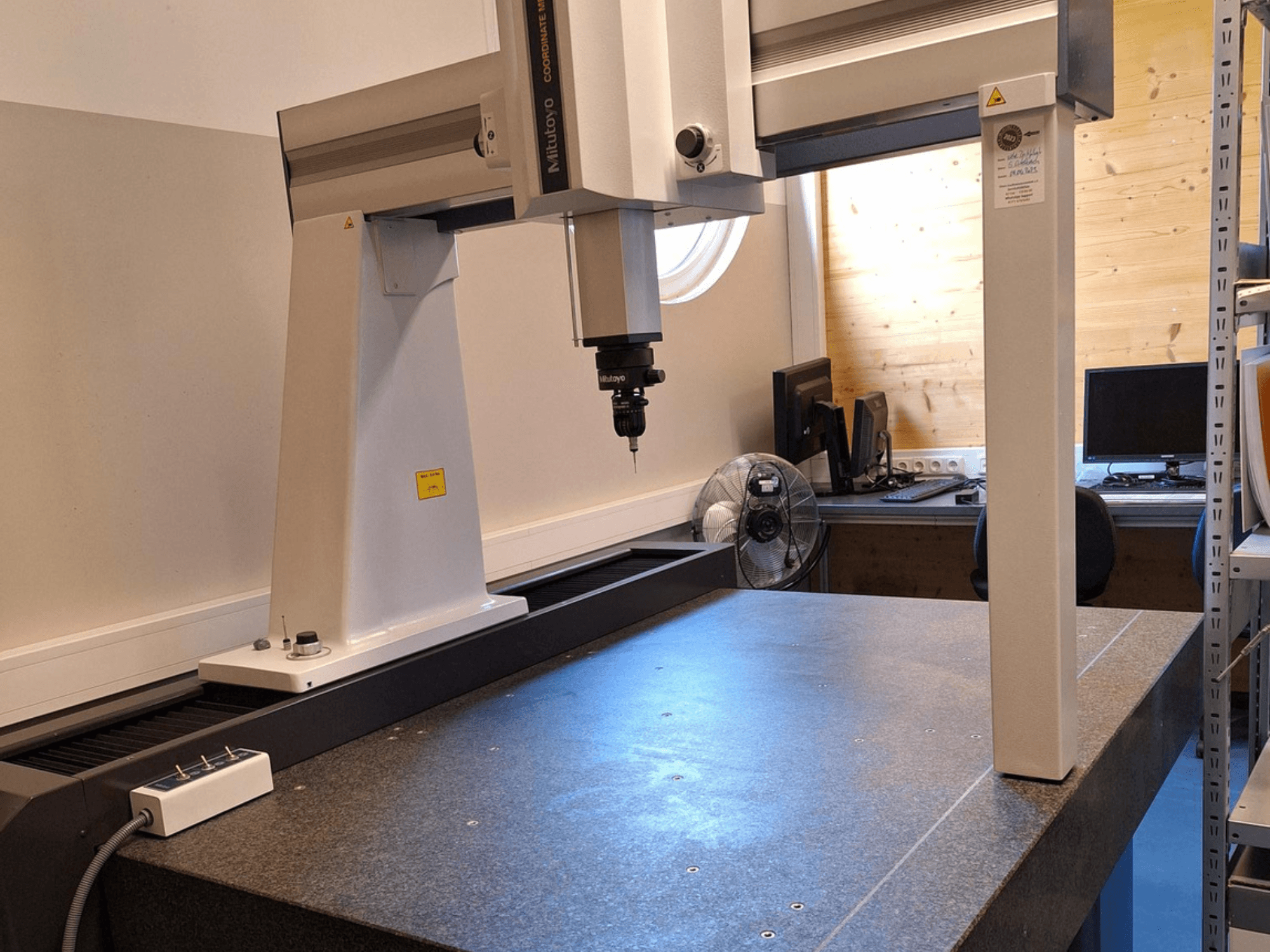 Robot a portale Mitutoyo Crysta-Plus M7106 in un'officina, vista frontale, con sonda di misura e piastra di appoggio in granito.