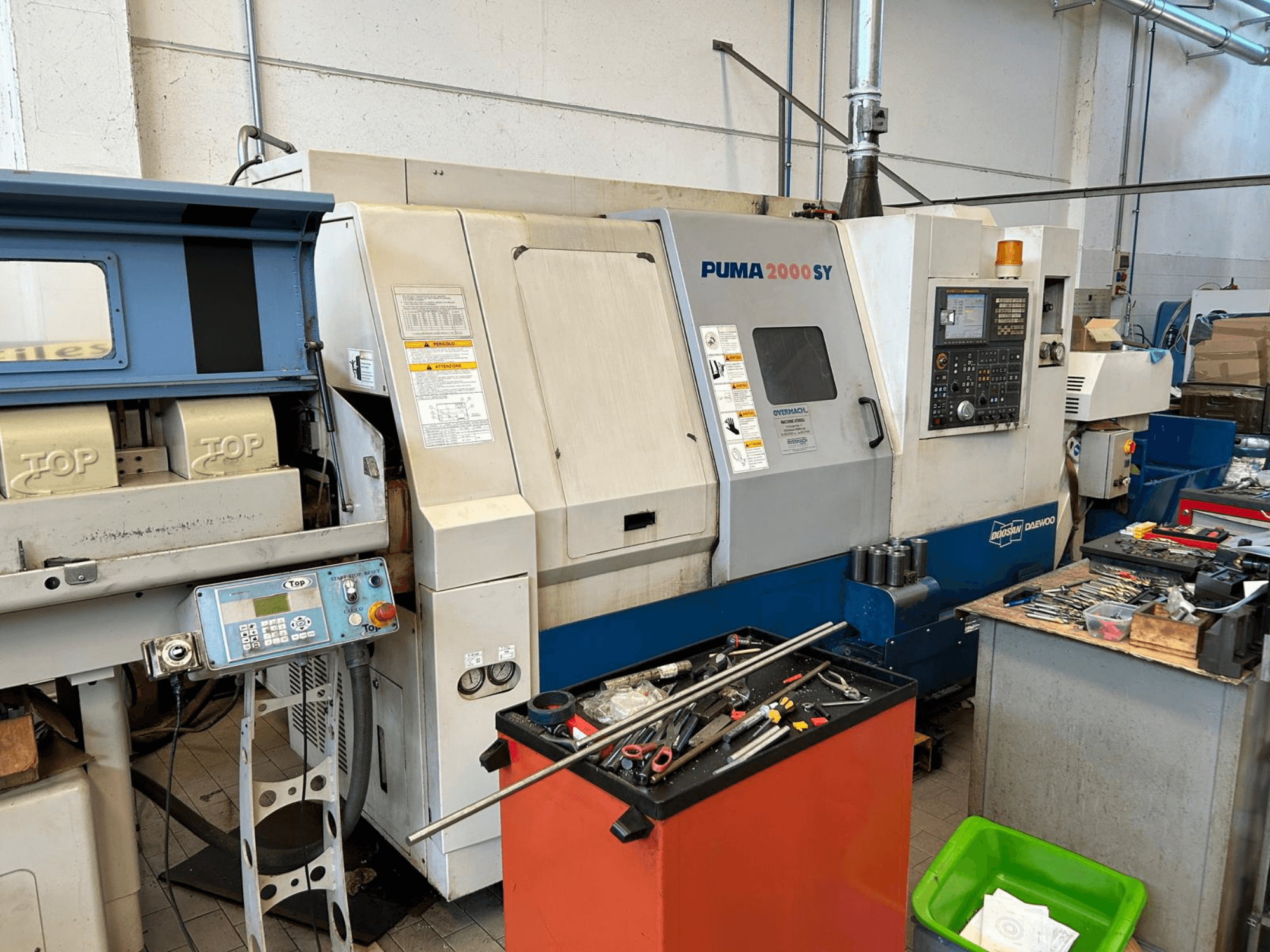 Tornio orizzontale DOOSAN PUMA 2000SY in un’officina; vista laterale che mostra il pannello di controllo e gli utensili nelle vicinanze.