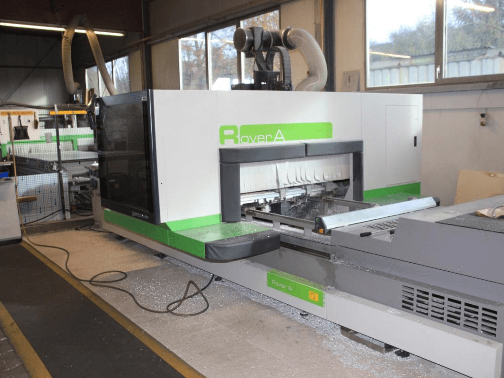 Router CNC BIESSE Rover A 1232, vista laterale che mostra l'area di taglio e il pannello di controllo in un ambiente industriale.