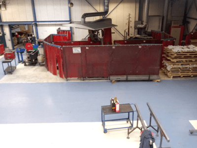 Spazio di lavoro industriale con tende rosse per la saldatura, macchine e pallet; vista dall'alto che mostra il layout e le attrezzature.