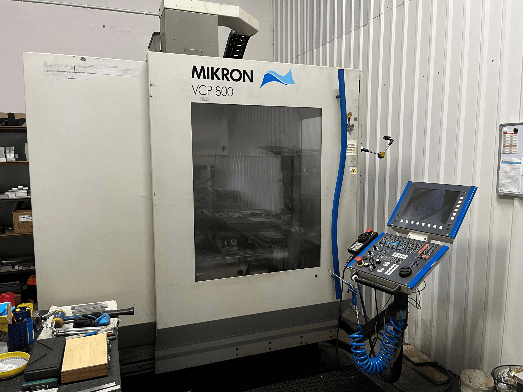 Centro di lavorazione verticale MIKRON VCP 800, vista frontale, con pannello di controllo e utensili su un banco da lavoro in primo piano.