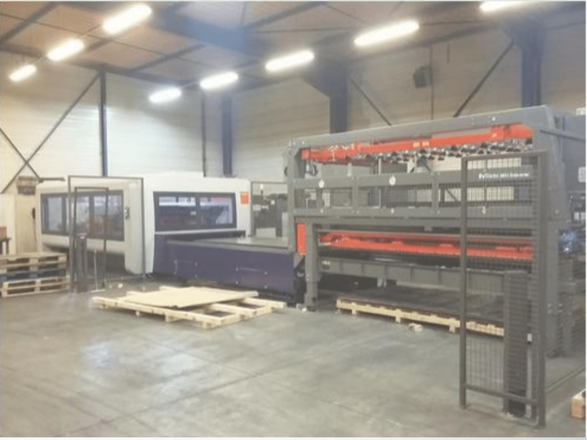 Allestimento di macchinari industriali in un magazzino; include una taglierina laser grigia e un router CNC viola, vista frontale con pallet.