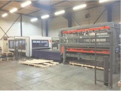 Allestimento di macchinari industriali in un magazzino; include una taglierina laser grigia e un router CNC viola, vista frontale con pallet.